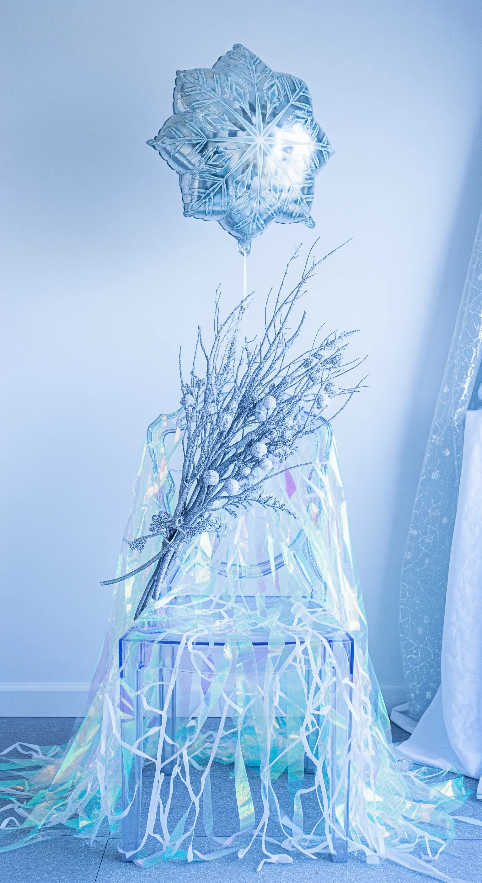 Sedia trasparente coperta da un telo iridescente, con rami argentati e palloncino a fiocco di neve.