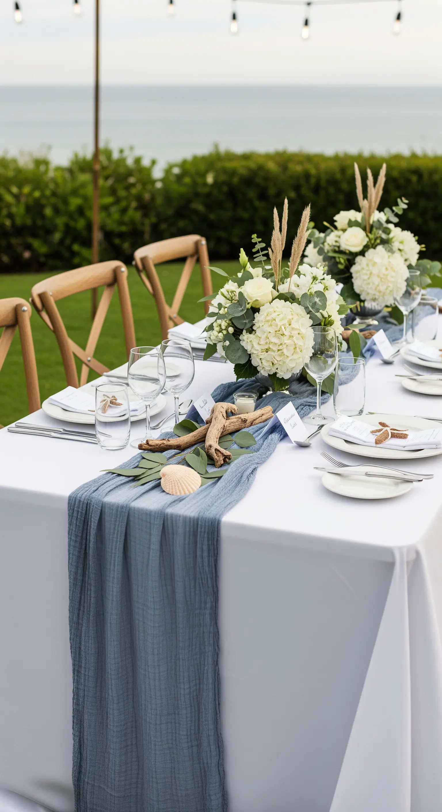 Tavola da matrimonio vista mare con runner blu polvere, ortensie bianche e decorazioni marine.
