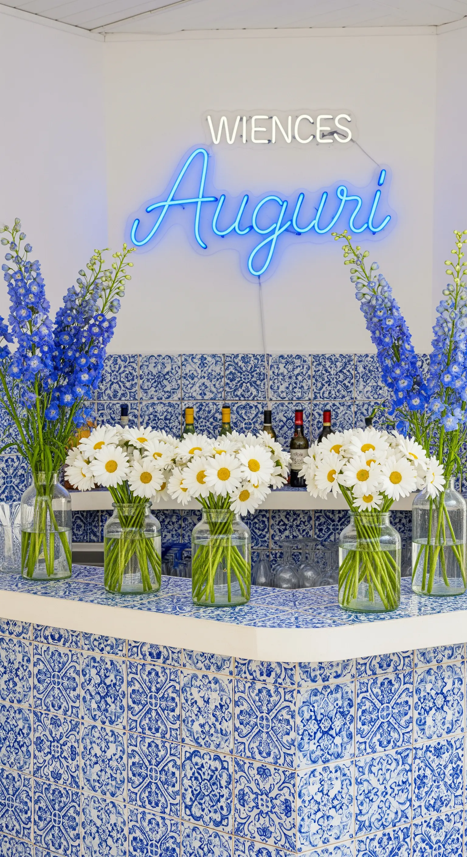 Bar con piastrelle blu e bianche, vasi di margherite e insegna 