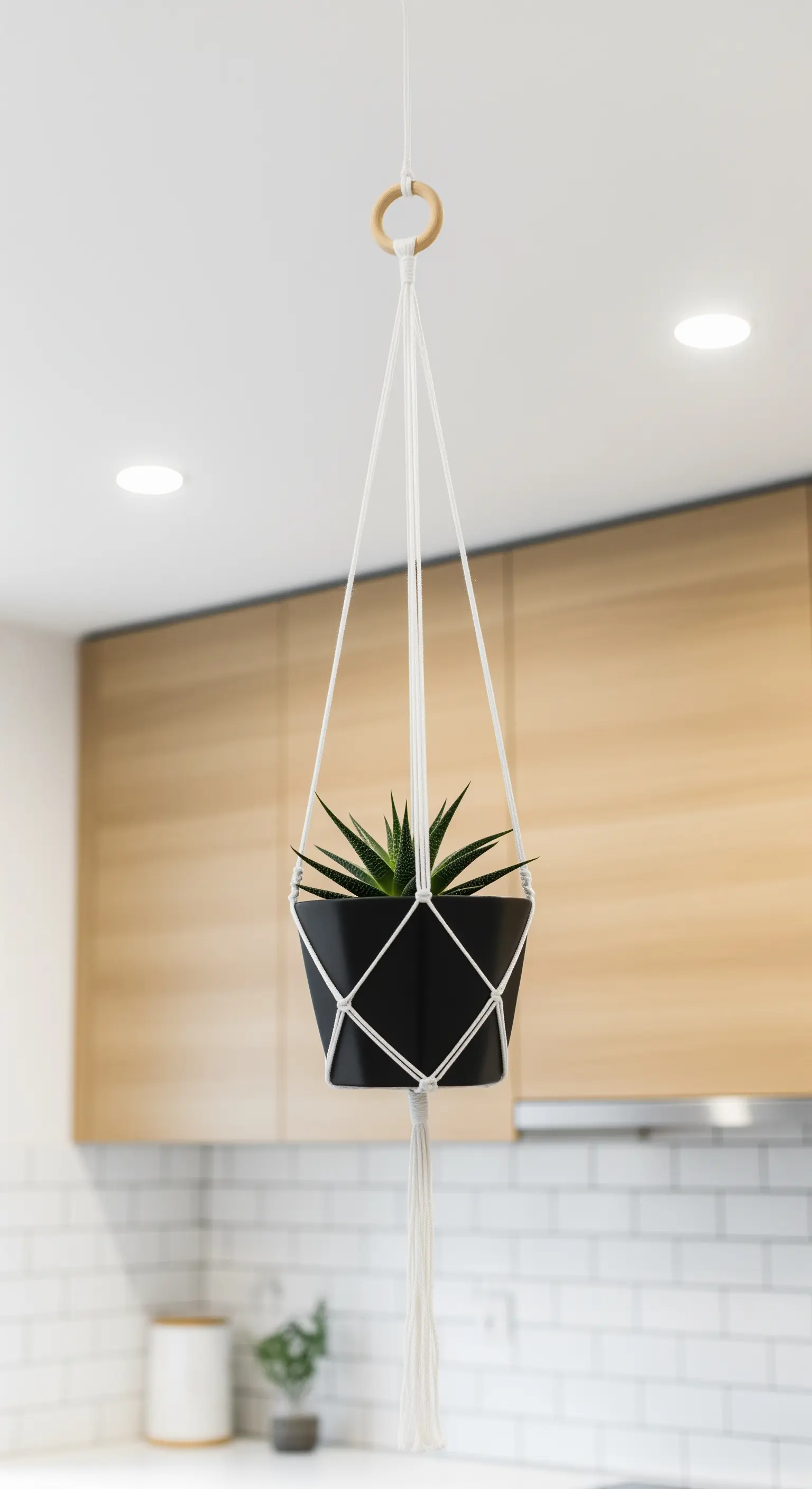 Portavasi in macramè bianco con vaso nero, sospeso in una cucina moderna con mobili in legno.