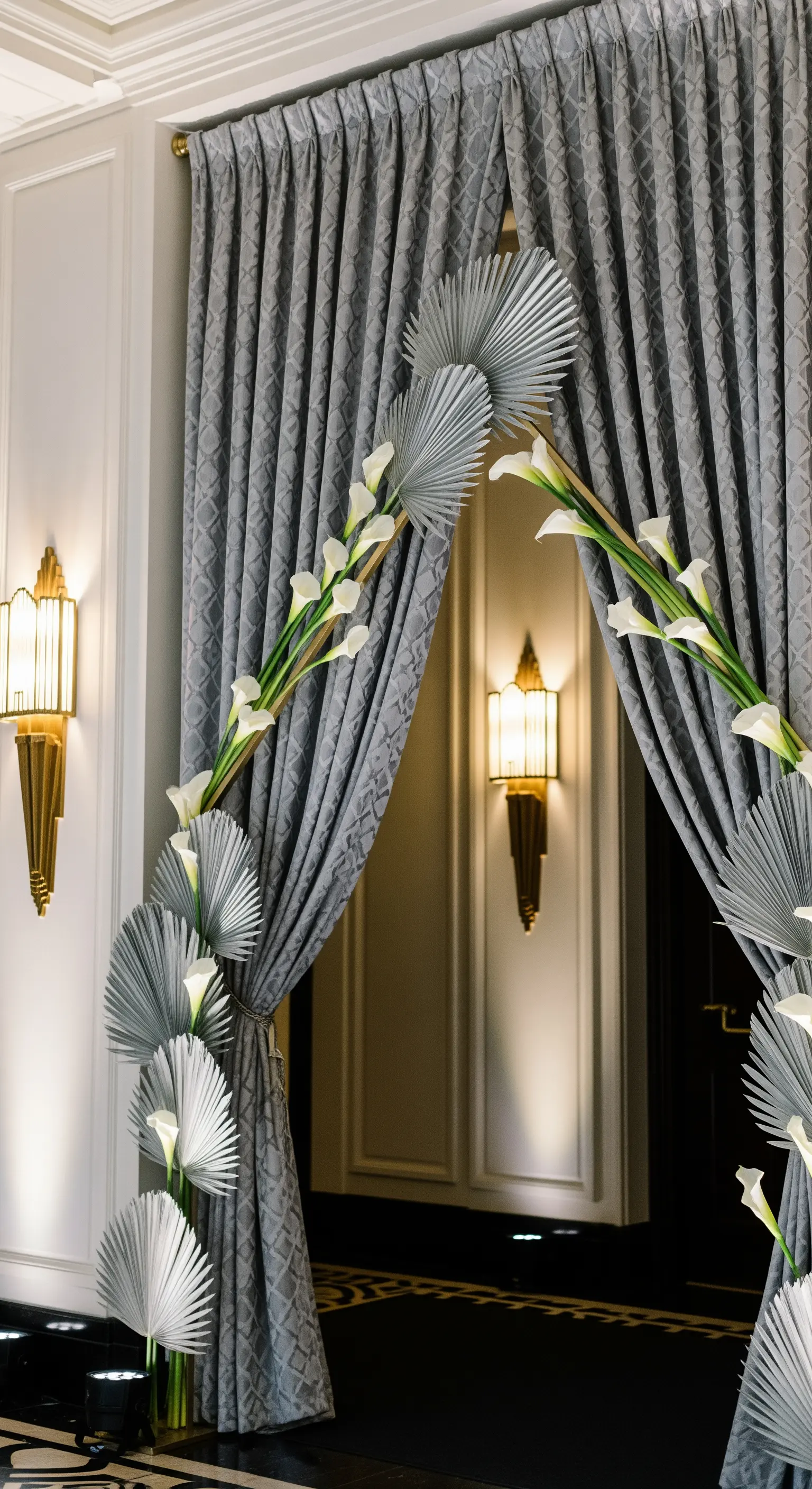 Ingresso moderno con tende grigie e decorazioni con foglie di palma argentate e calle bianche.