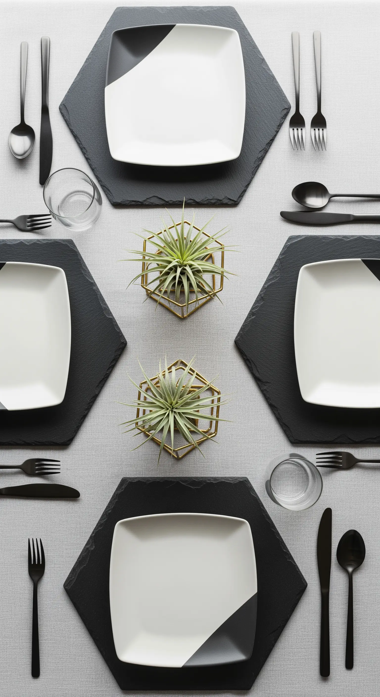 Tavola con tovagliette esagonali, piatti bicolore e piante aeree in supporti dorati.