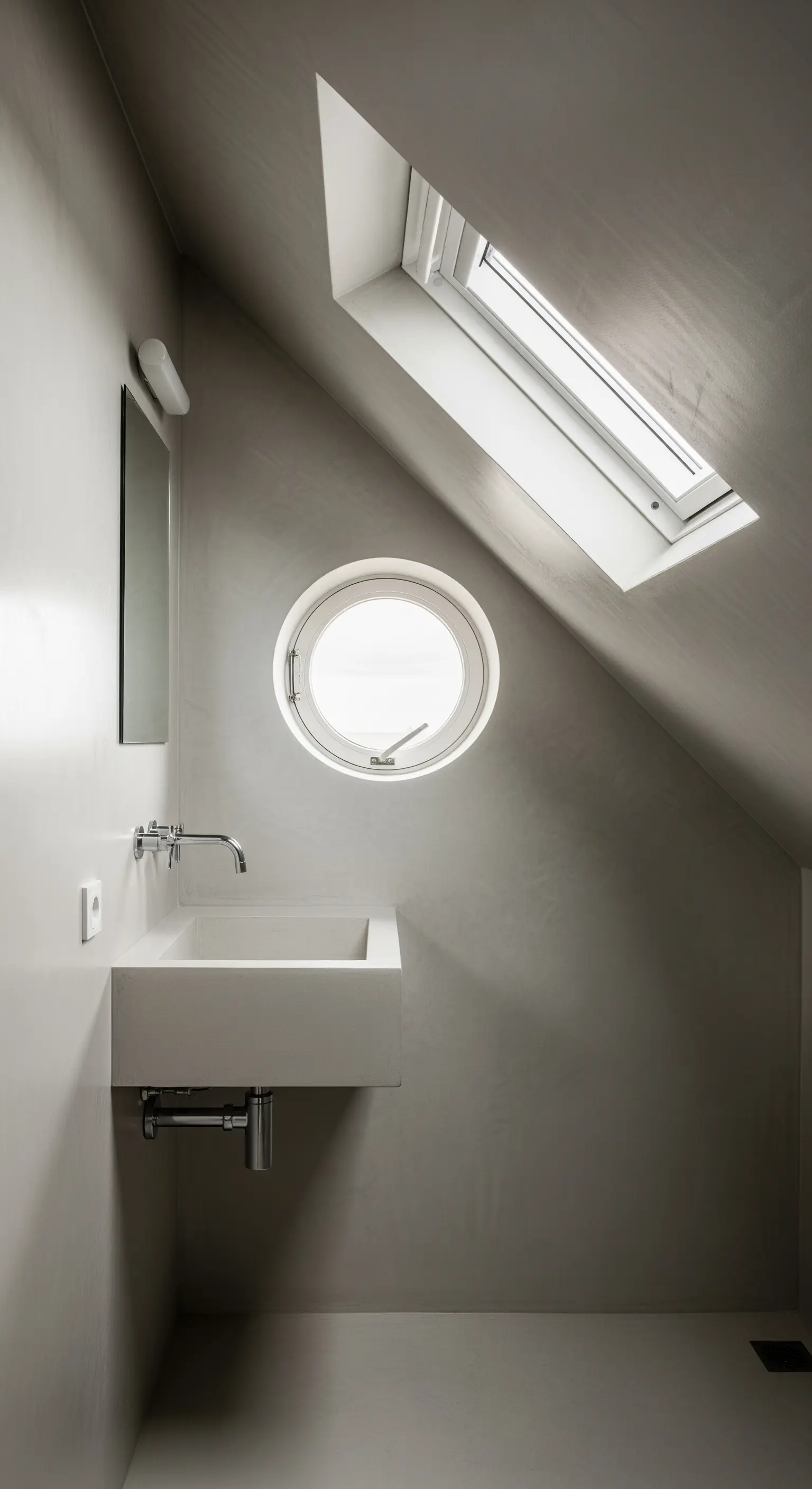 Bagno minimalista in mansarda con pareti e pavimento continui e finestra a oblò.