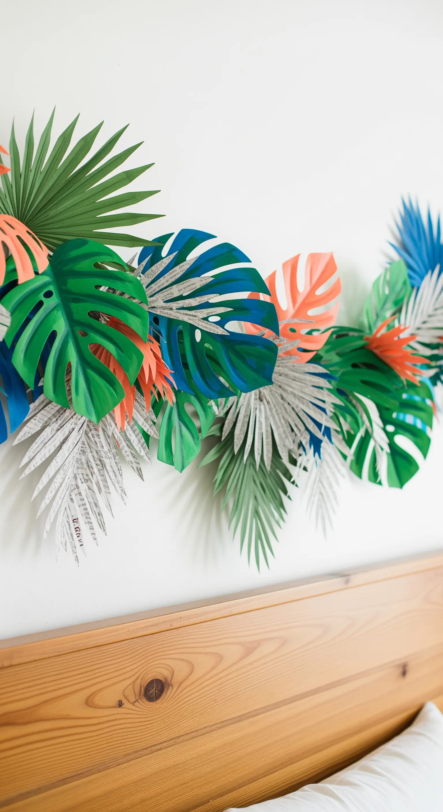 Foglie tropicali di carta, alcune colorate e altre di giornale, disposte sopra una testiera in legno.