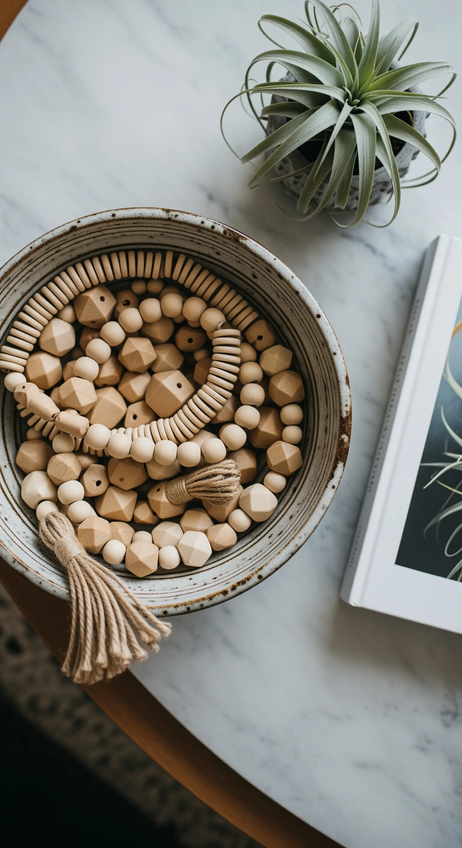 Ciotola in ceramica su un tavolo di marmo, riempita con ghirlande di perline di legno grezzo.