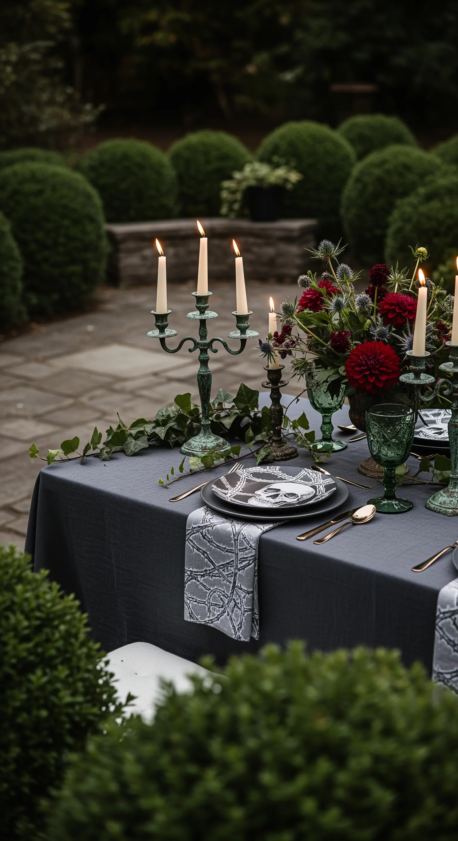 Tavola elegante in giardino con candelabri verderame e fiori rossi scuri.