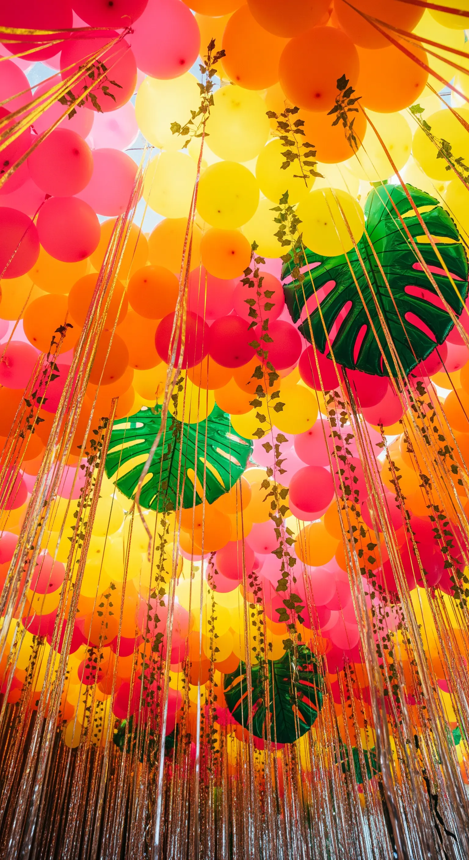 Soffitto coperto di palloncini rosa e gialli, con foglie di monstera e fili dorati.