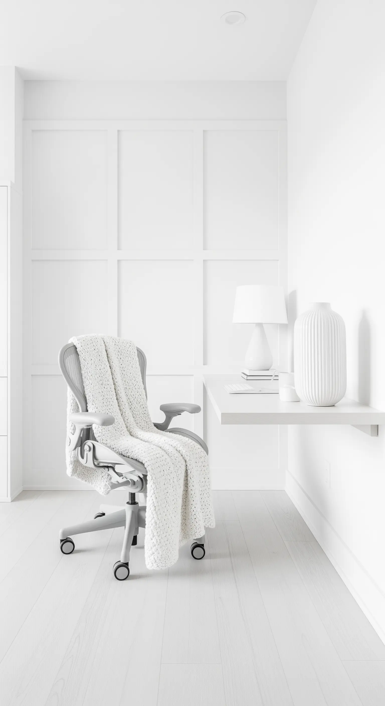 Home office monocromatico total white con sedia ergonomica coperta da un plaid a maglia grossa.