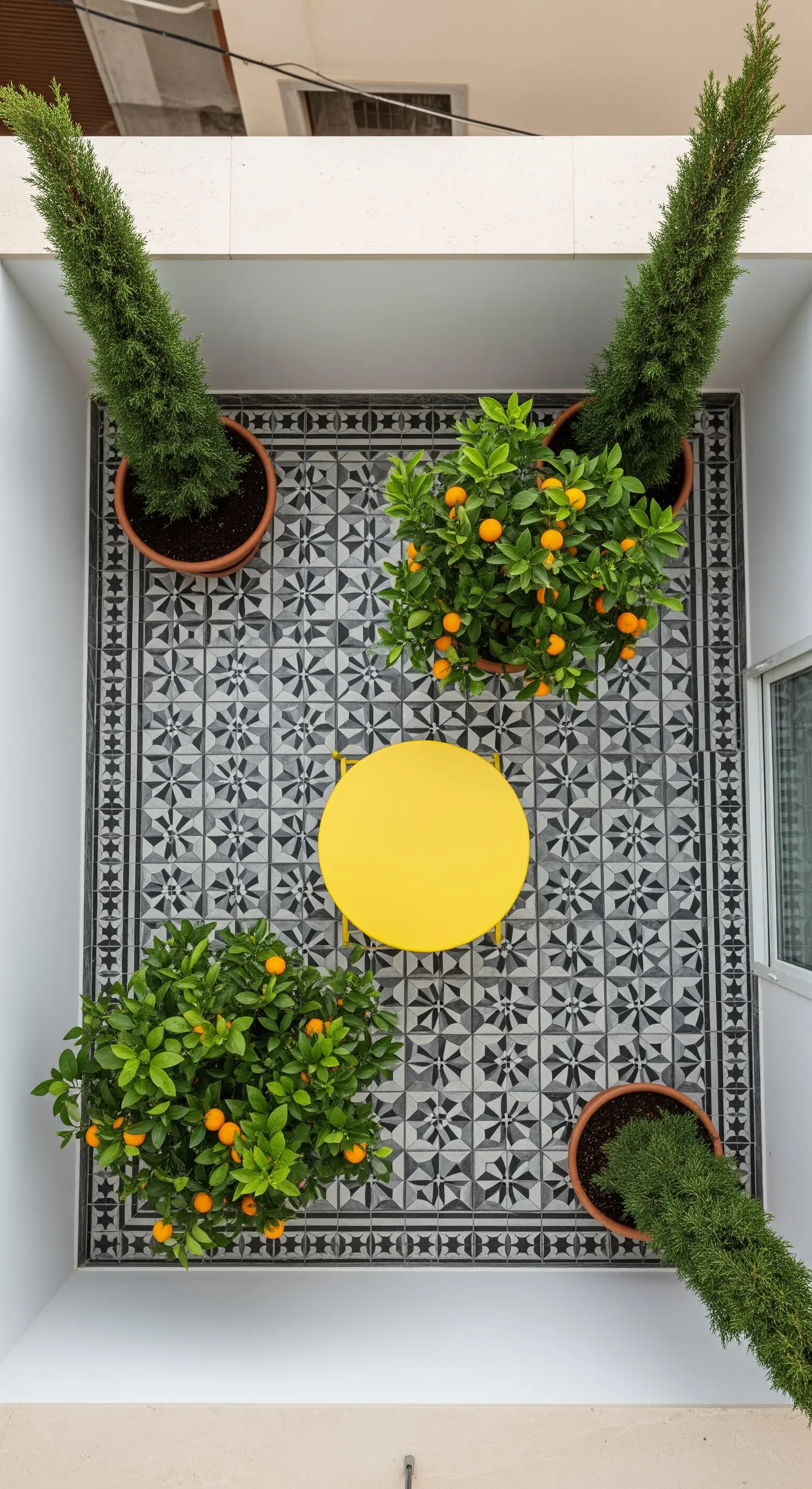 Vista dall'alto di un piccolo patio con piastrelle geometriche bianche e nere e un tavolo giallo