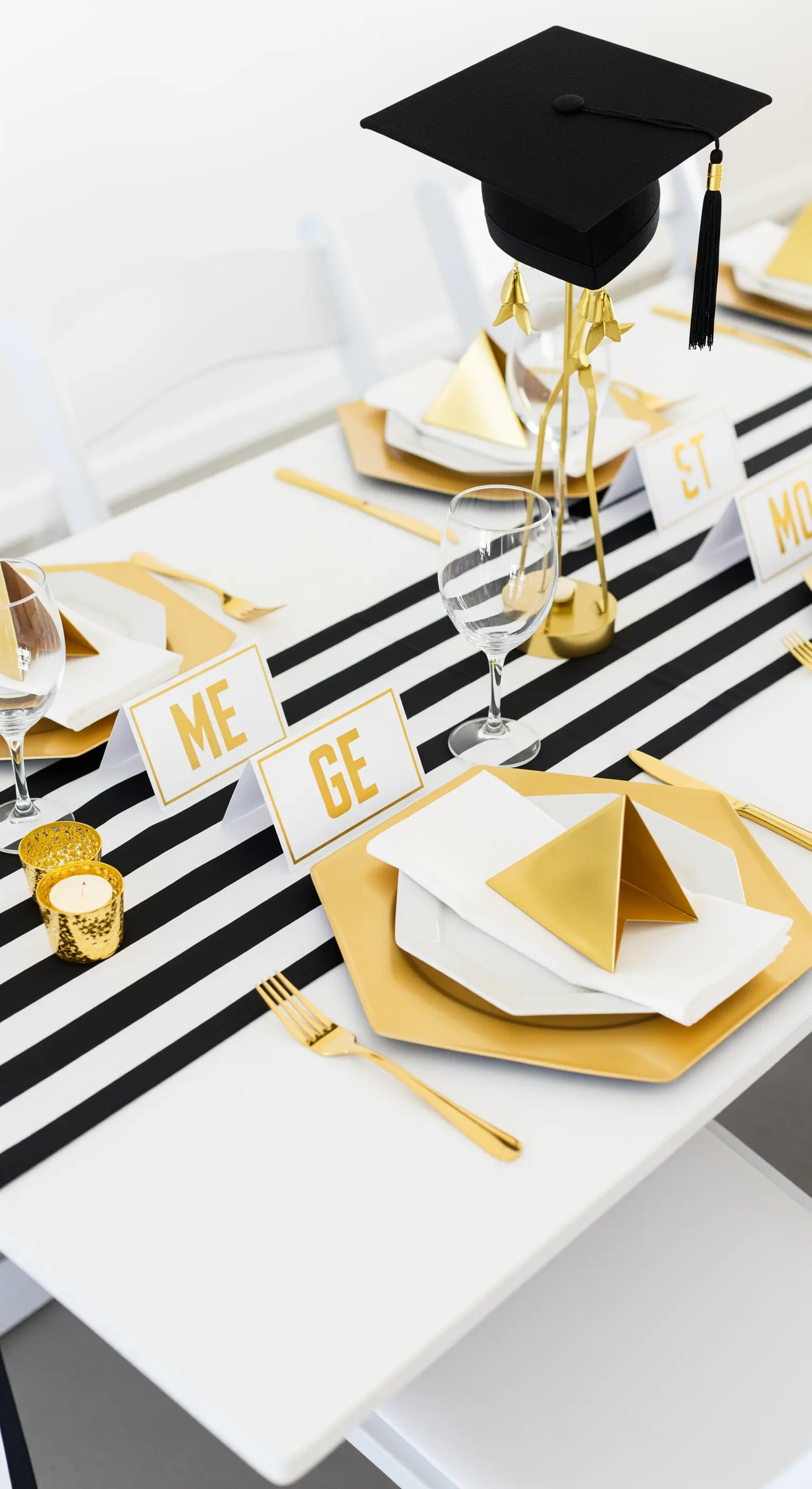 Tavola a tema laurea con runner a righe bianche e nere, piatti e dettagli dorati.