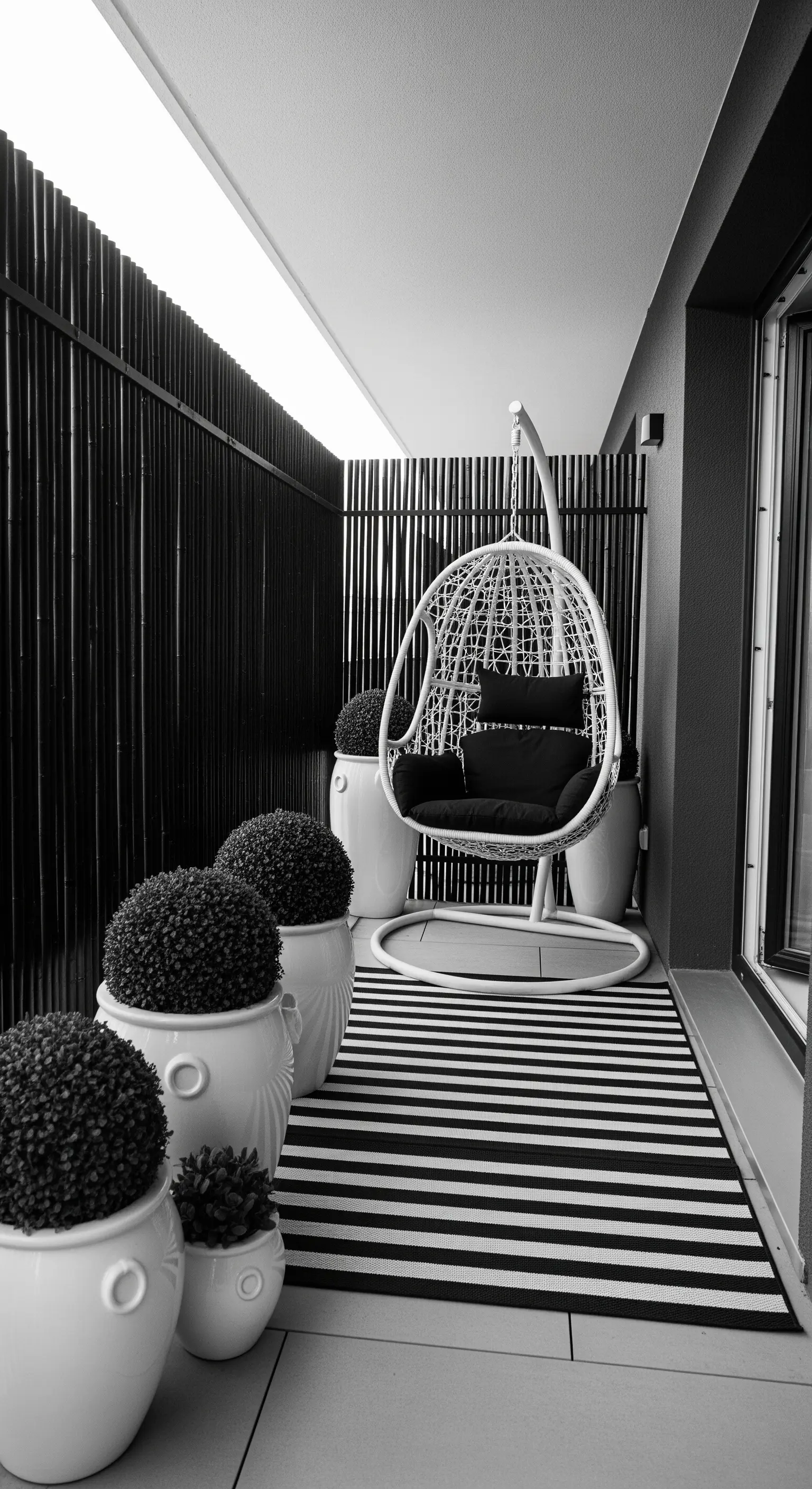Balcone elegante in bianco e nero con poltrona sospesa e tappeto a righe.