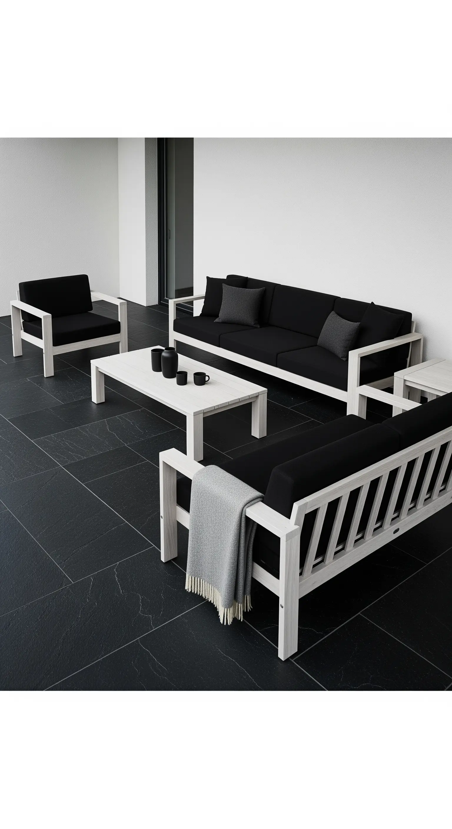 Set di arredi da esterno in legno bianco e cuscini neri su pavimento in ardesia scura.