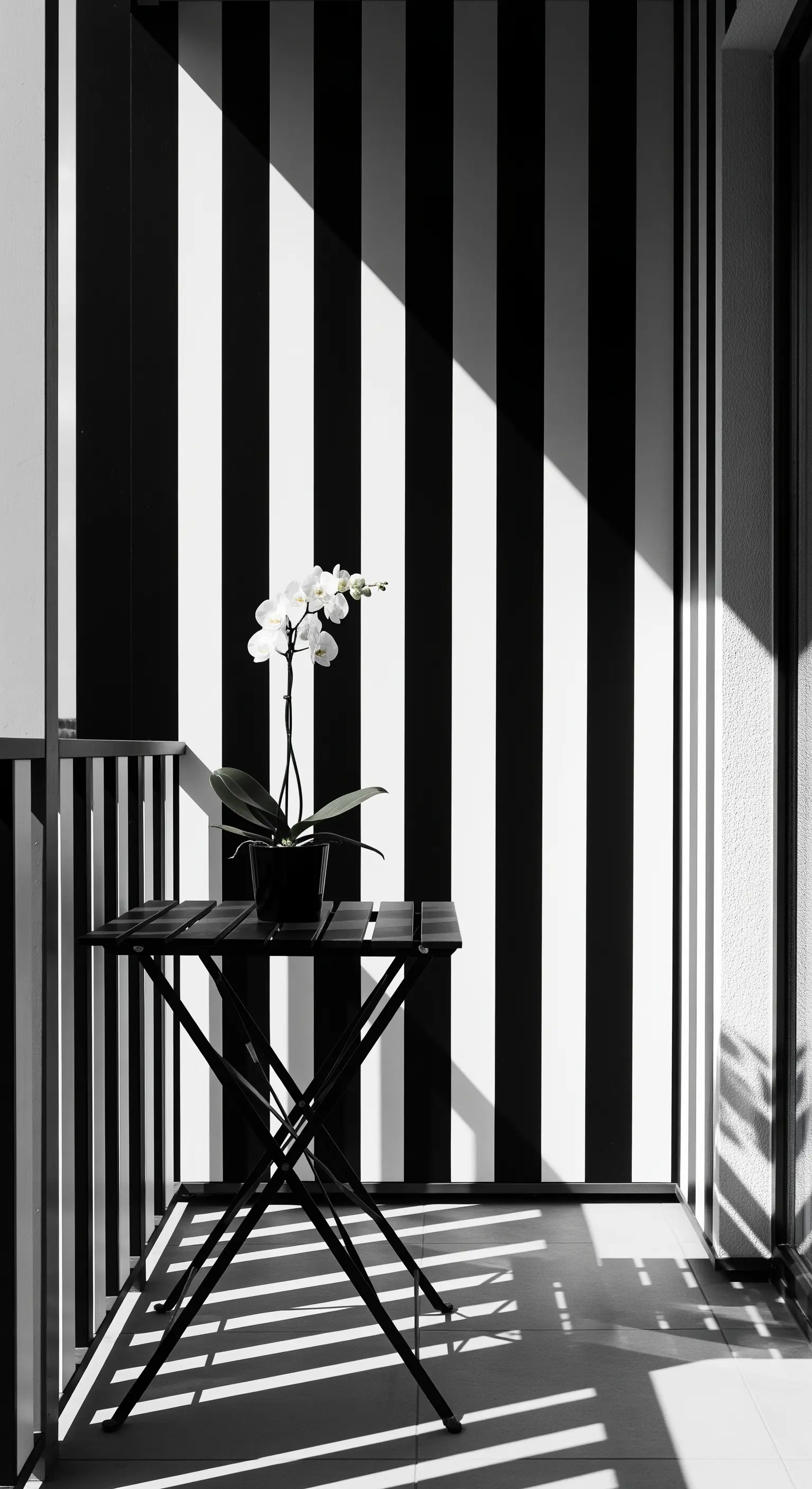 Balcone minimalista con parete a righe larghe bianche e nere e un'orchidea su un tavolino.