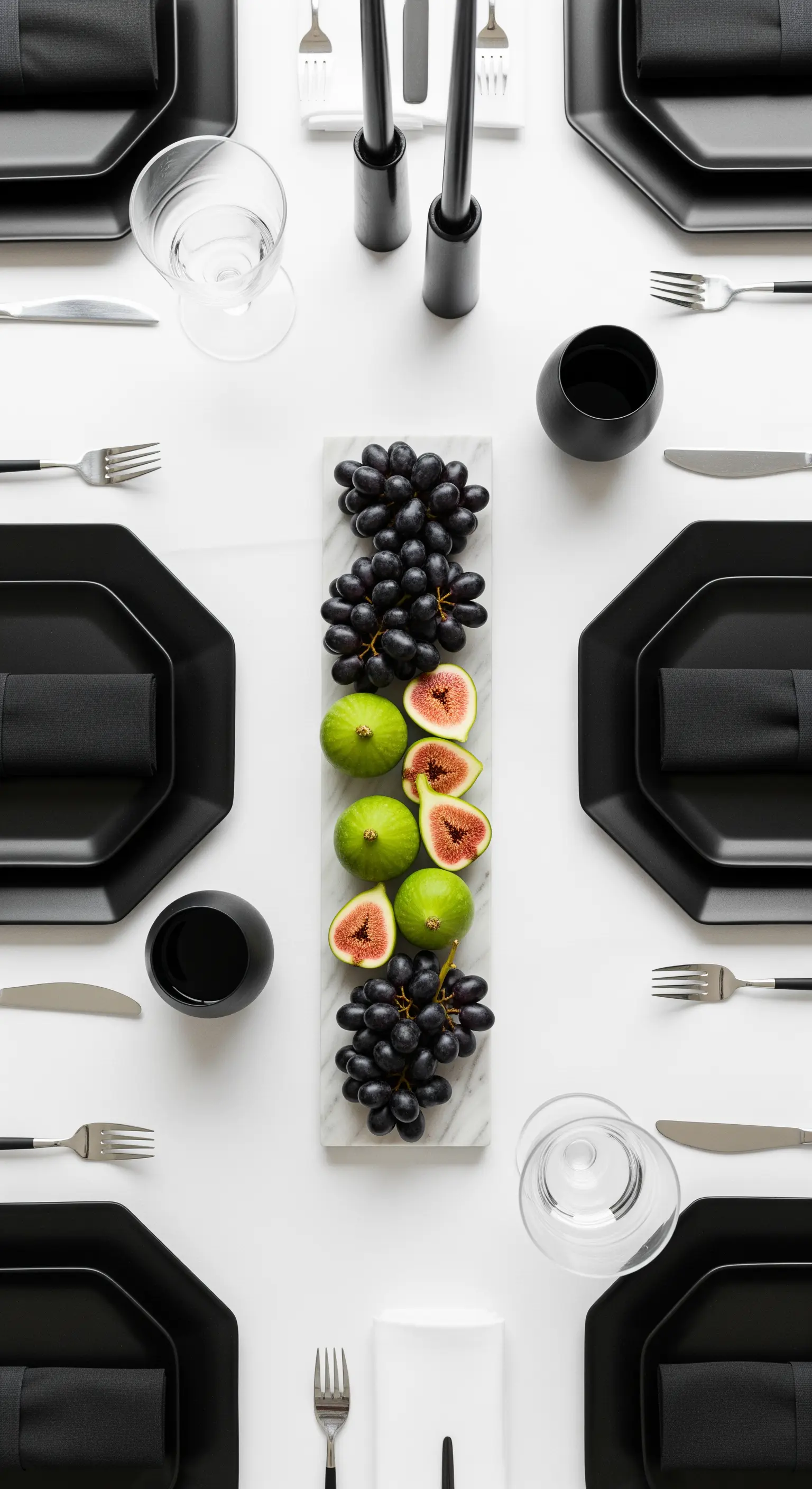 Tavola in bianco e nero con frutta scura su un vassoio di marmo.