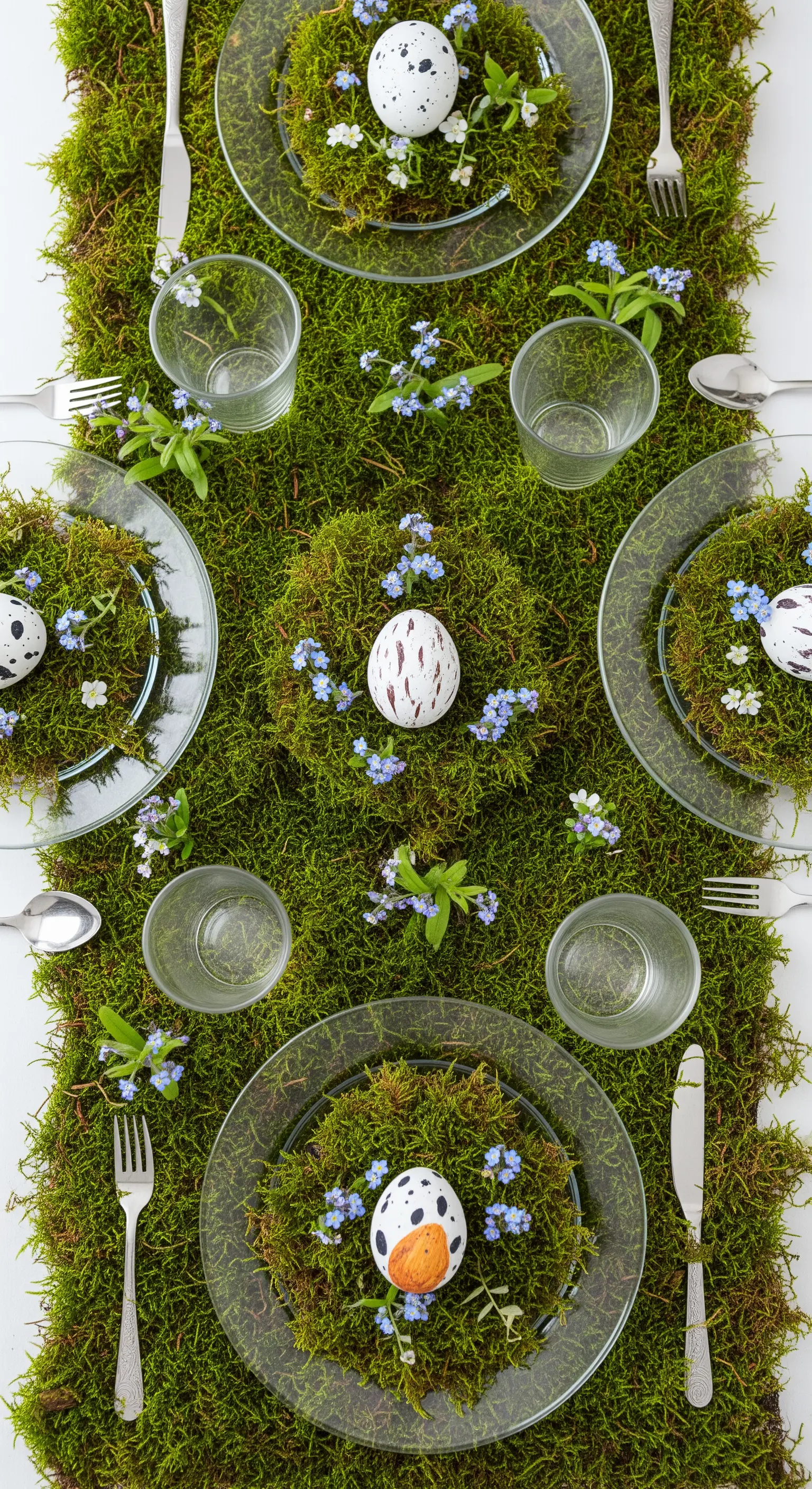 Runner da tavola fatto di muschio verde, con uova e piccoli fiori blu per Pasqua.