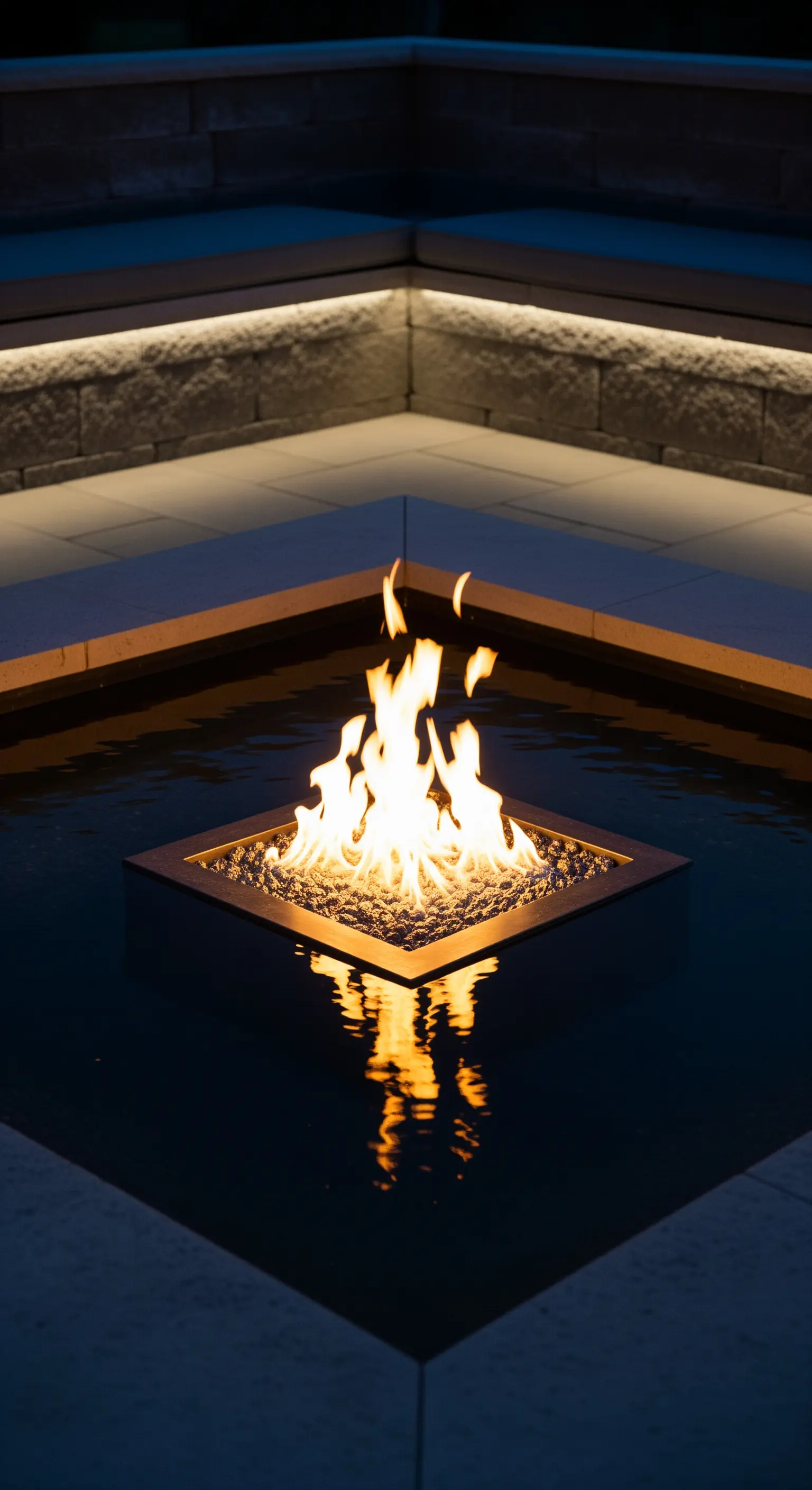 Braciere quadrato acceso al centro di una vasca d'acqua scura in un patio moderno.