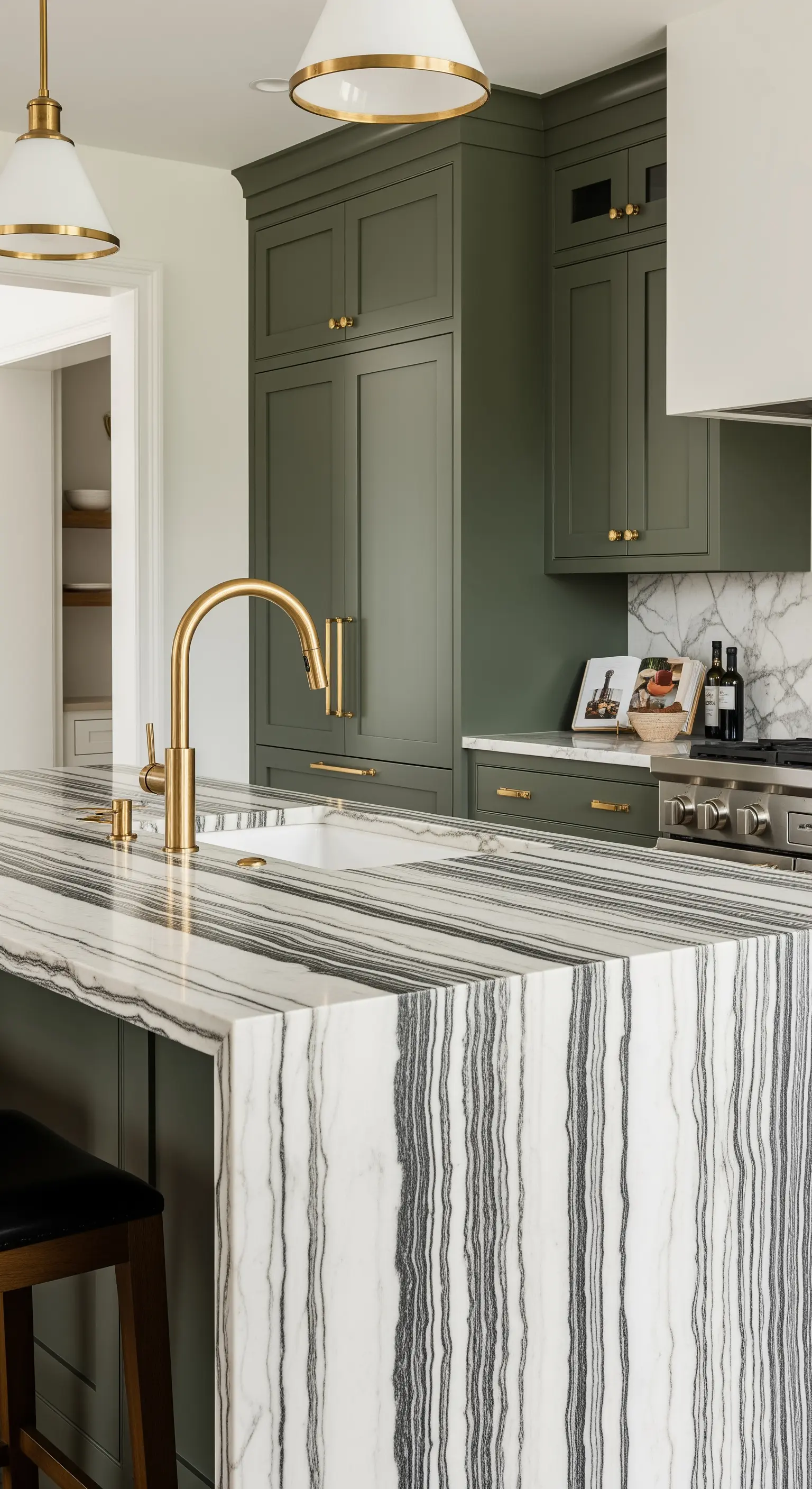 Isola cucina con fianchi rivestiti in marmo con venature verticali, abbinata a mobili color verde oliva.