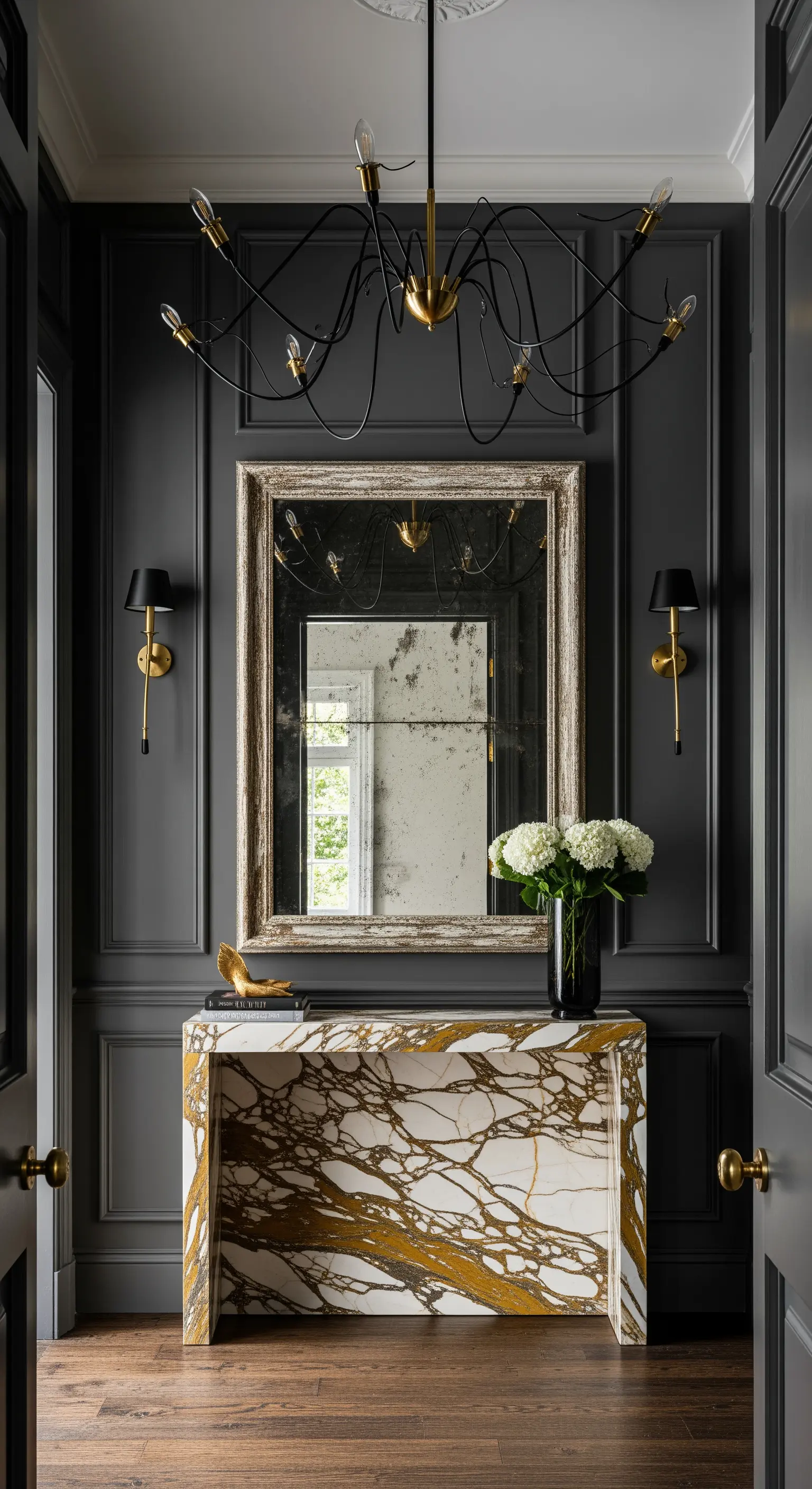 Ingresso con boiserie grigio scuro, specchio anticato e consolle in marmo con venature dorate.