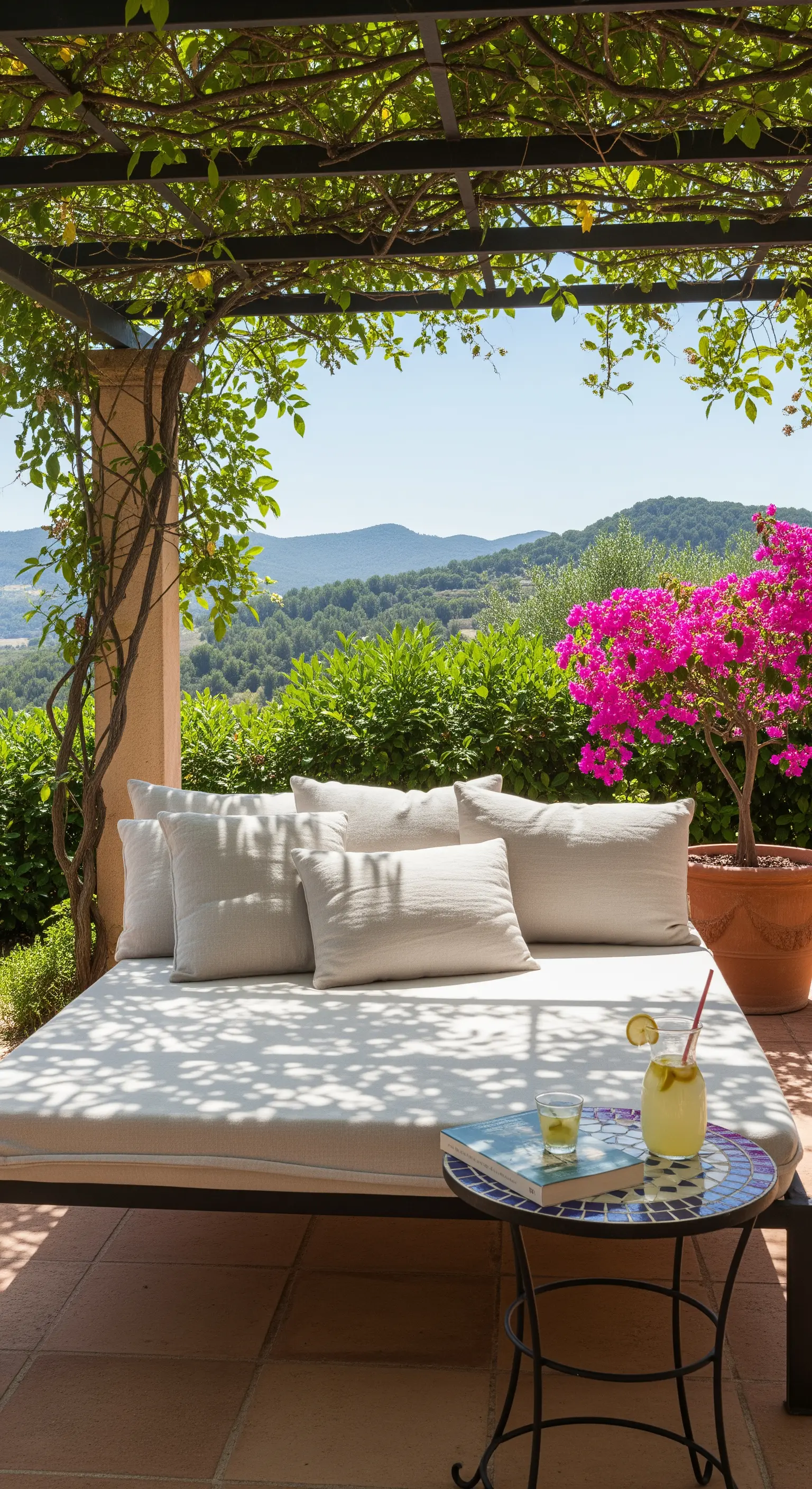 Terrazza ombreggiata con un daybed, cuscini chiari e un tavolino in mosaico.