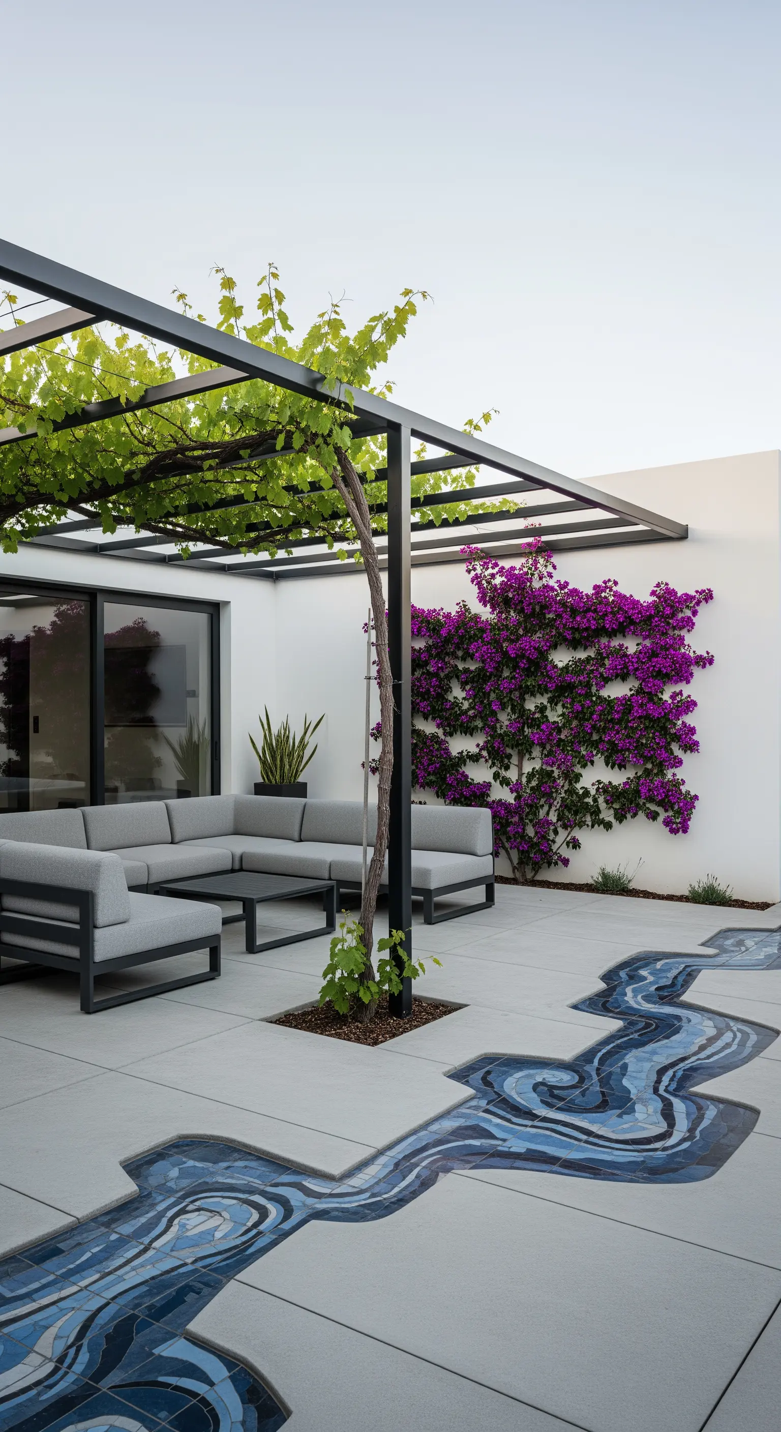 Patio moderno con pergola nera, divano grigio e un mosaico a forma di fiume sul pavimento.