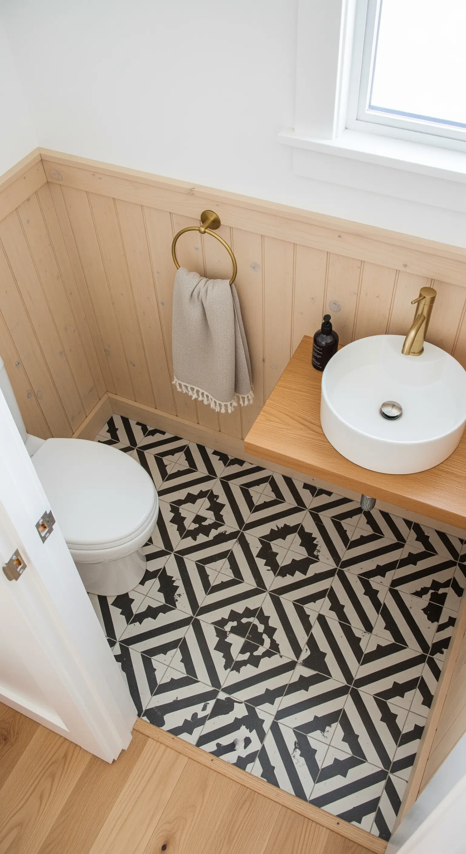 Bagno piccolo con boiserie in legno chiaro e piastrelle grafiche in bianco e nero.