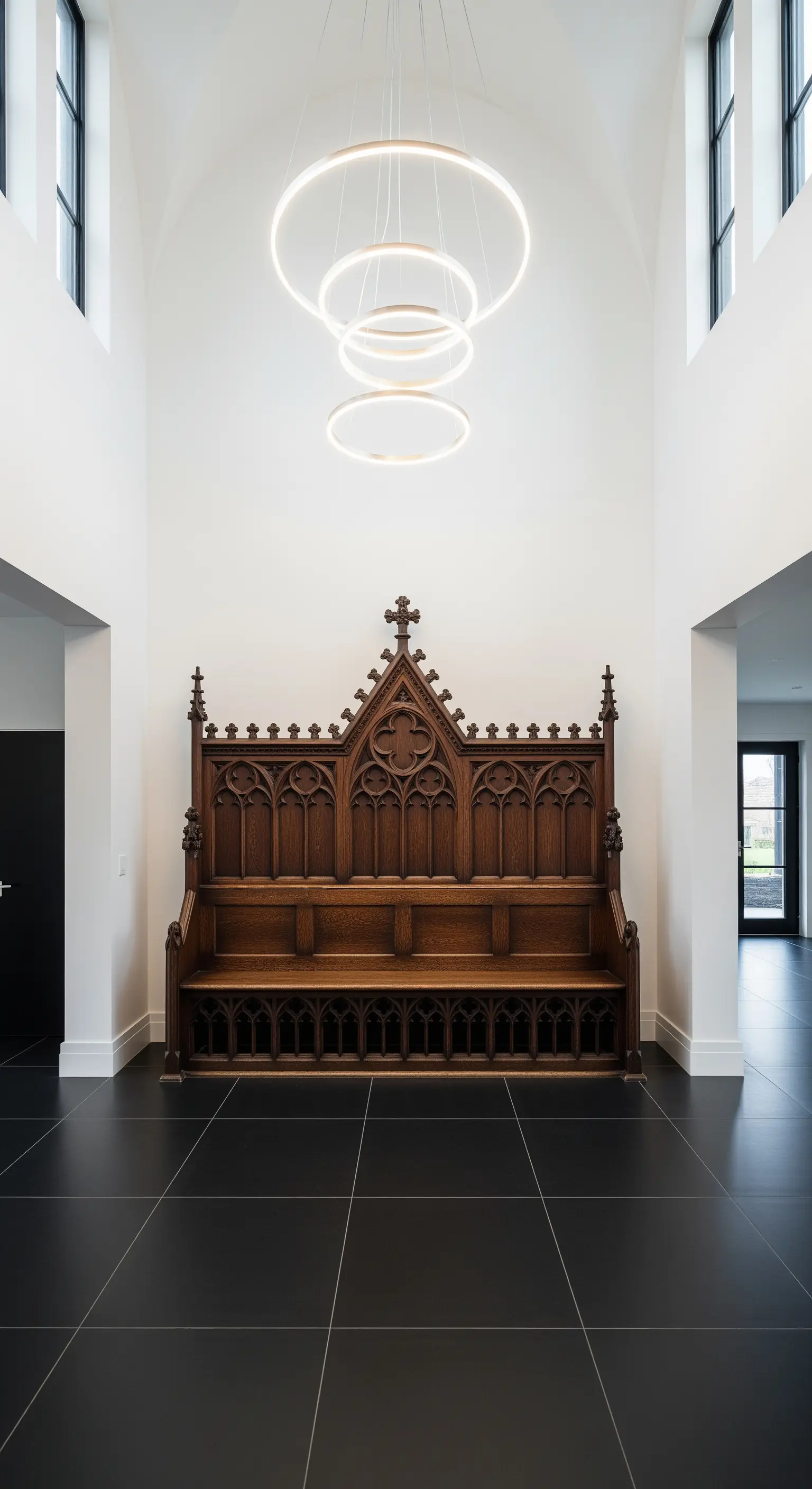 Panca neogotica in legno scuro in un atrio bianco minimale con lampadario a LED circolare.