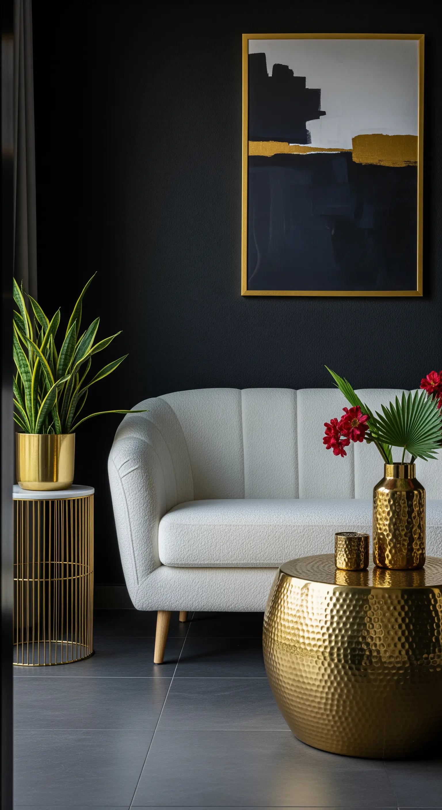 Divanetto bianco davanti a una parete nera, con tavolini e vaso dorati e un quadro astratto.