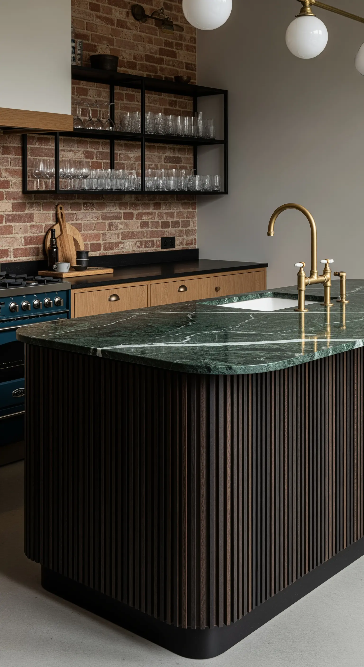 Isola con top in marmo verde foresta e base cannettata in legno scuro, su sfondo di mattoni a vista.