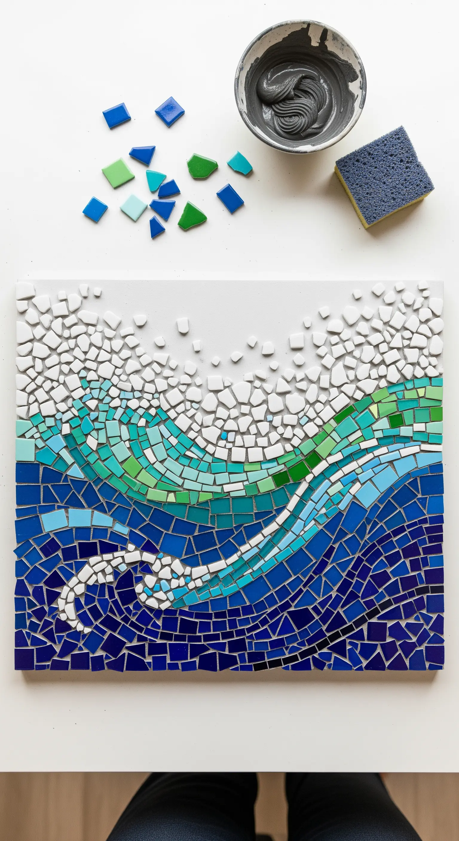 Mosaico di un'onda marina con tessere blu, verdi e bianche su un pannello bianco.