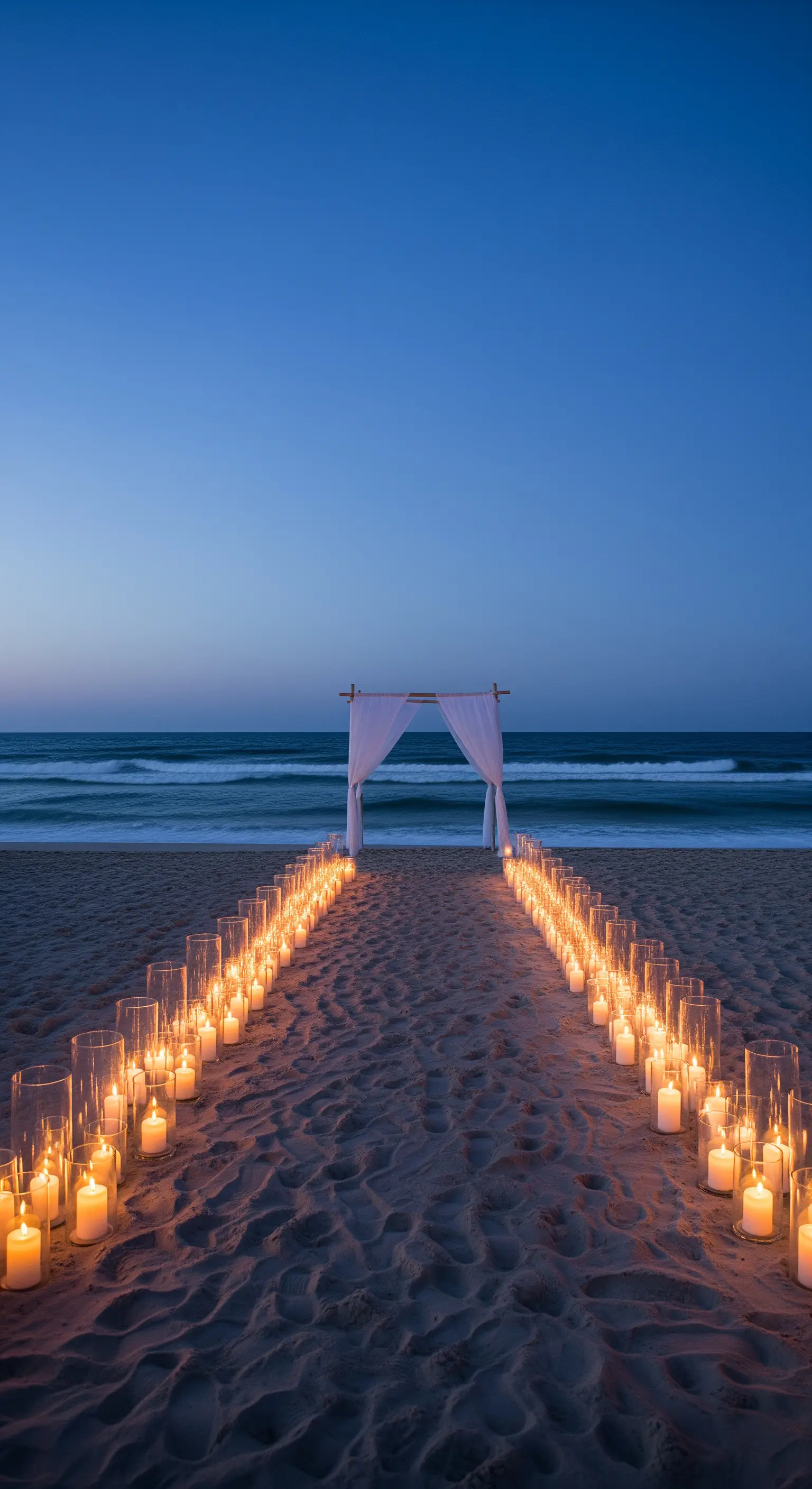 Percorso di candele nella sabbia che conduce a un arco bianco sulla riva del mare al crepuscolo.