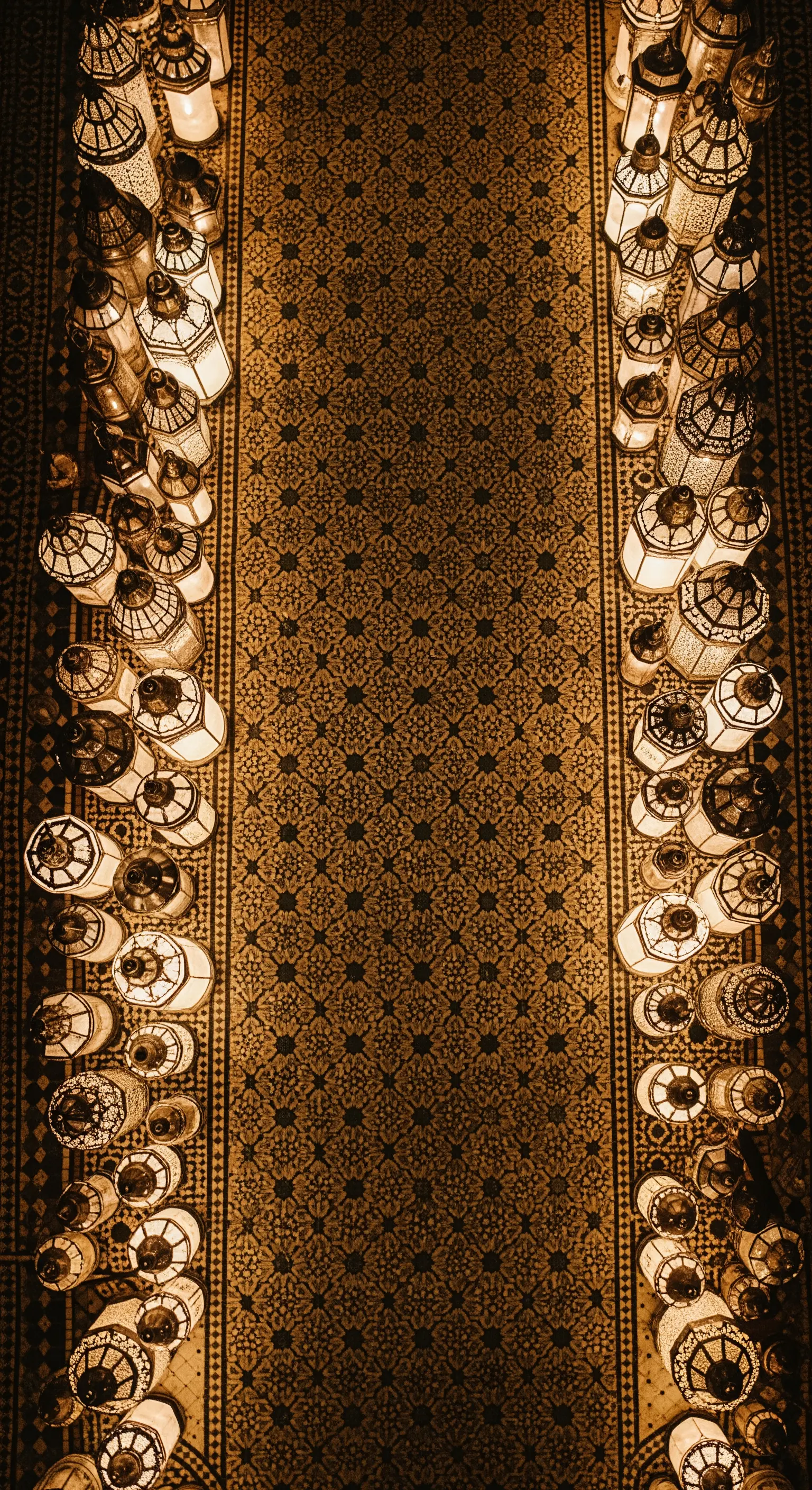 Vista dall'alto di un tappeto con pattern geometrico, i cui bordi sono delimitati da file di lanterne