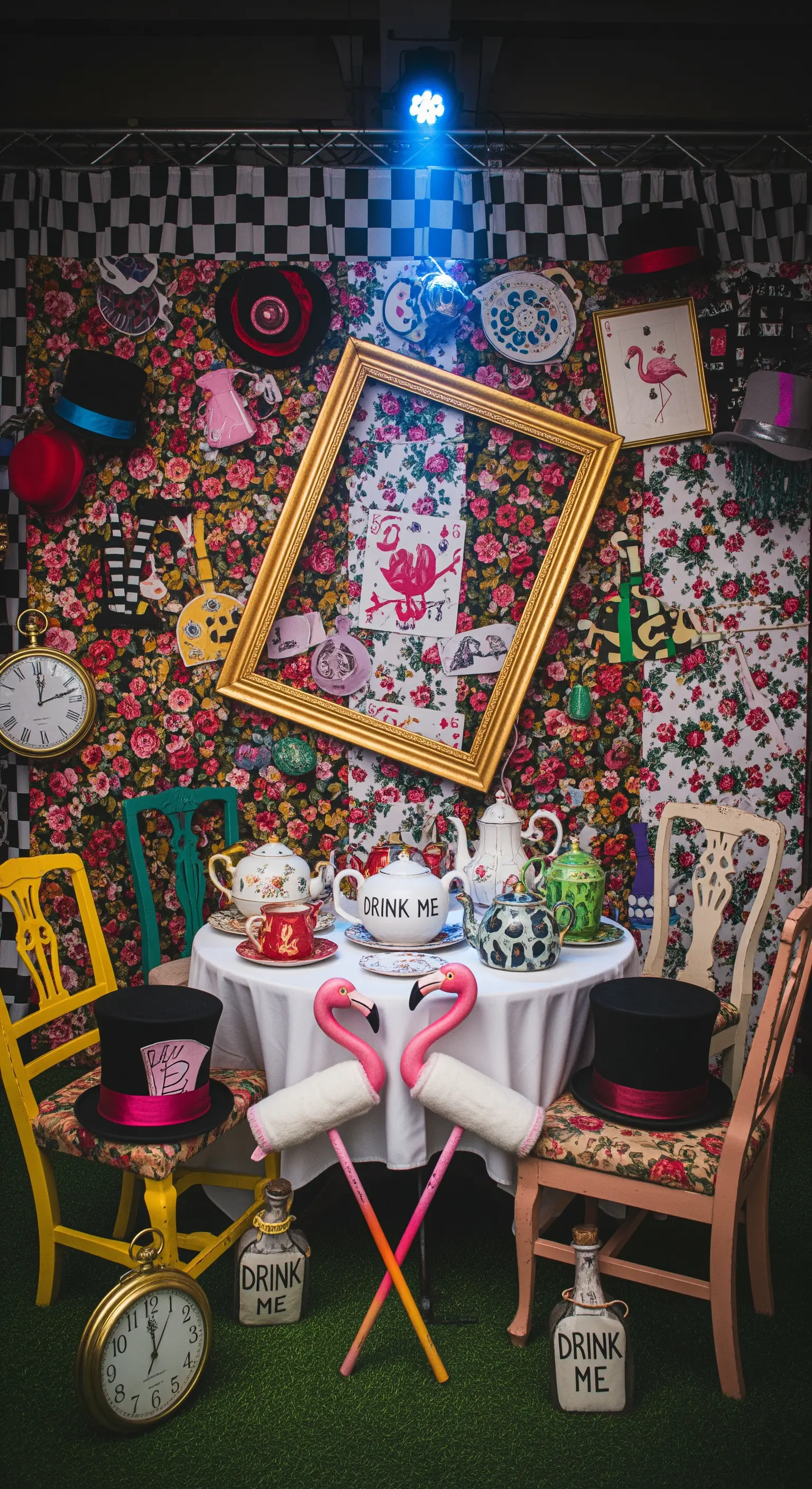 Photo booth a tema Alice nel Paese delle Meraviglie con un tavolo da tè, sedie spaiate e accessori surreali.