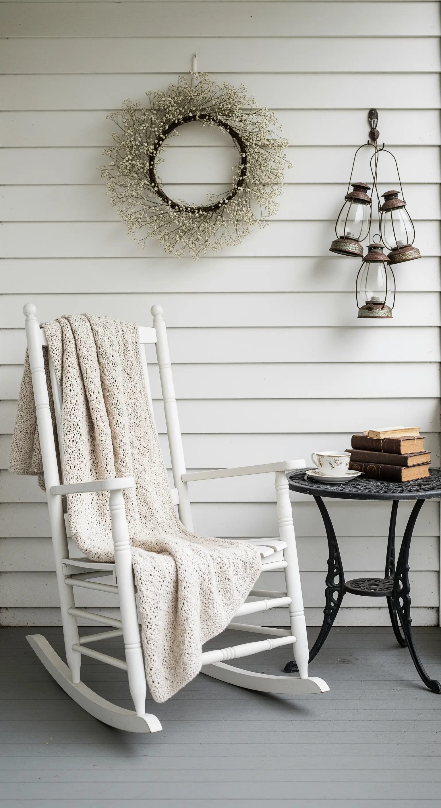 Sedia a dondolo bianca con coperta, ghirlanda di fiori secchi e lanterne decorative.
