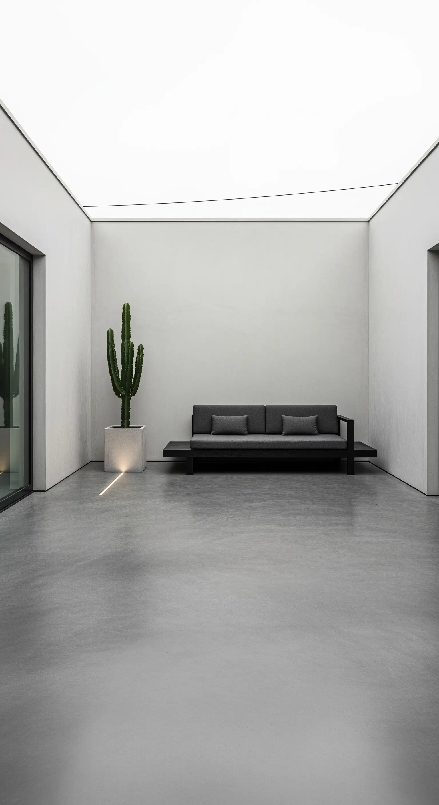 Patio minimalista con soffitto luminoso, divano grigio scuro e un cactus in un vaso bianco