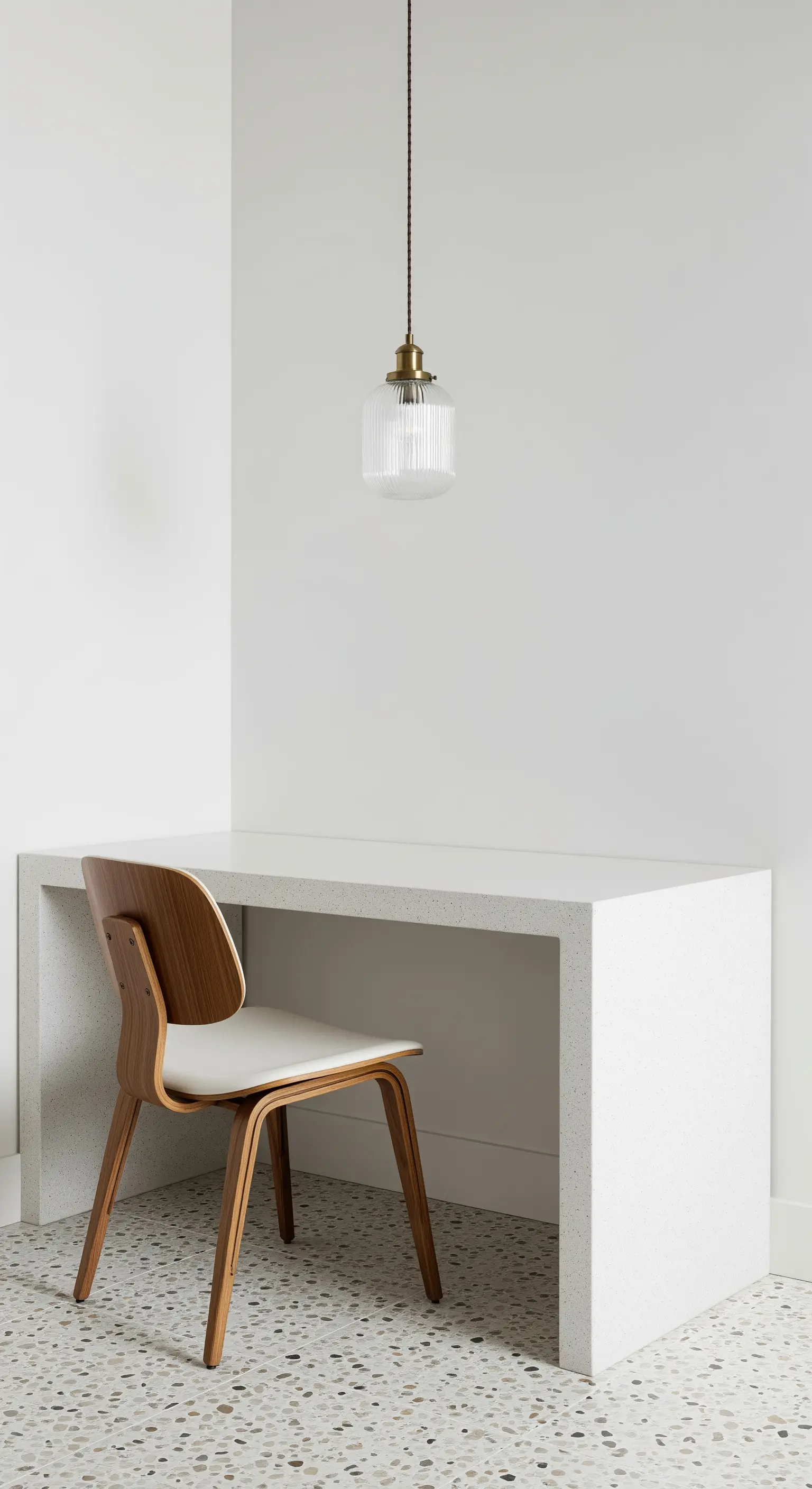 Scrivania minimale a cascata in terrazzo con sedia in legno e una lampada a sospensione in vetro.