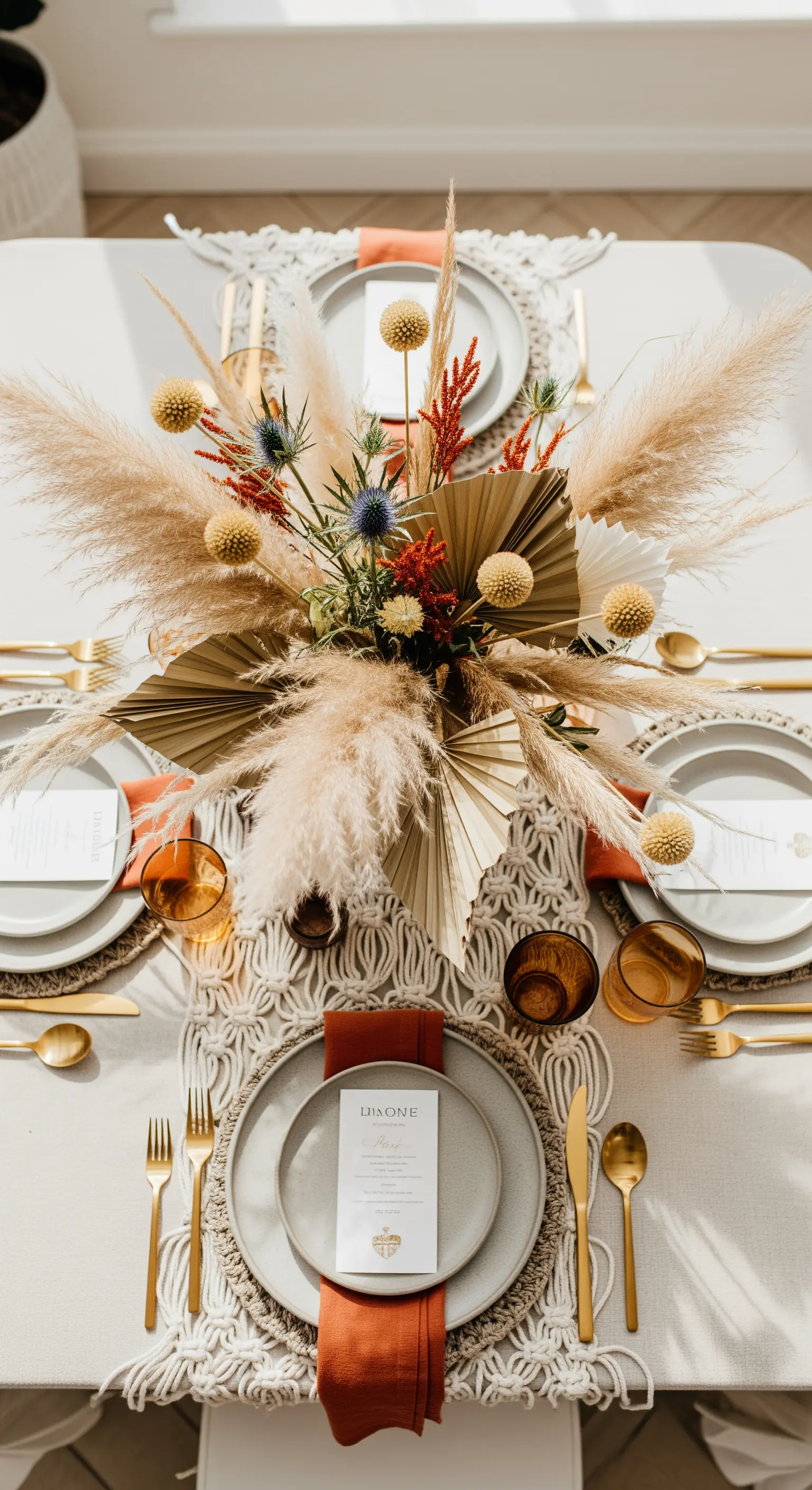 Mise en place boho chic con runner in macramè, pampas e posate dorate.