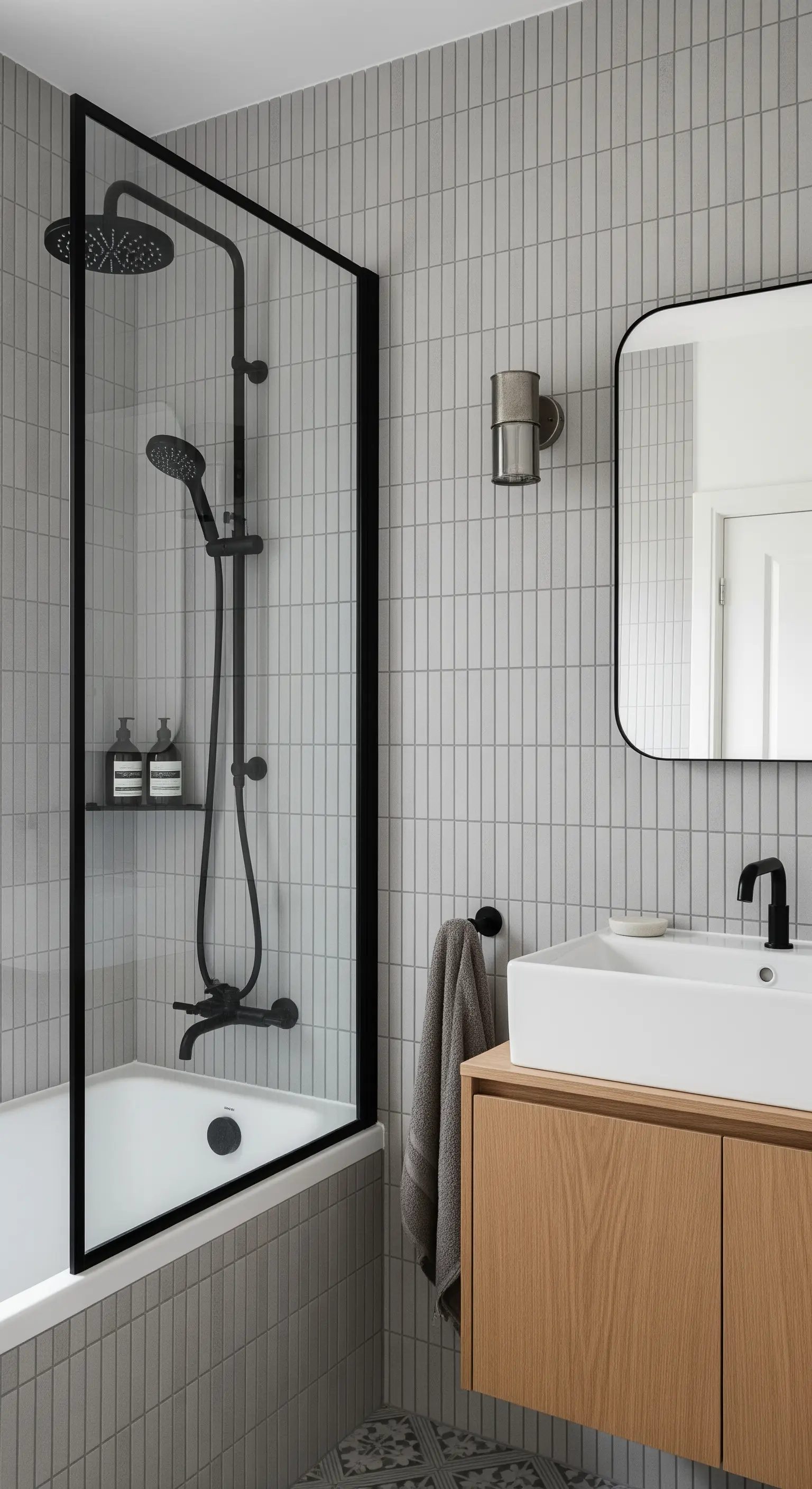 Bagno con piastrelle grigie verticali, box doccia con profili neri e mobile in legno.