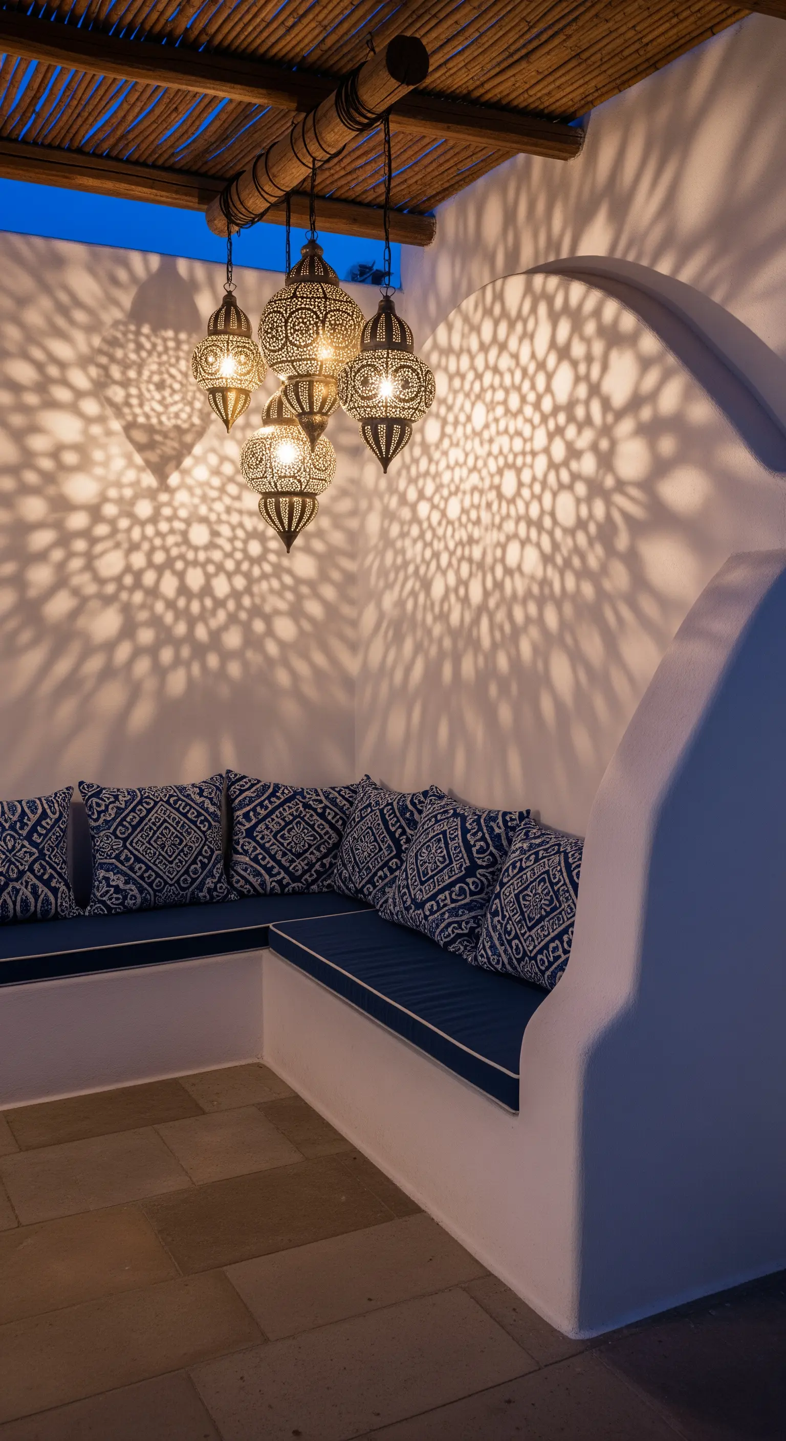Angolo relax in stile marocchino con seduta in muratura, cuscini blu e un lampadario che proietta ombre decorative.