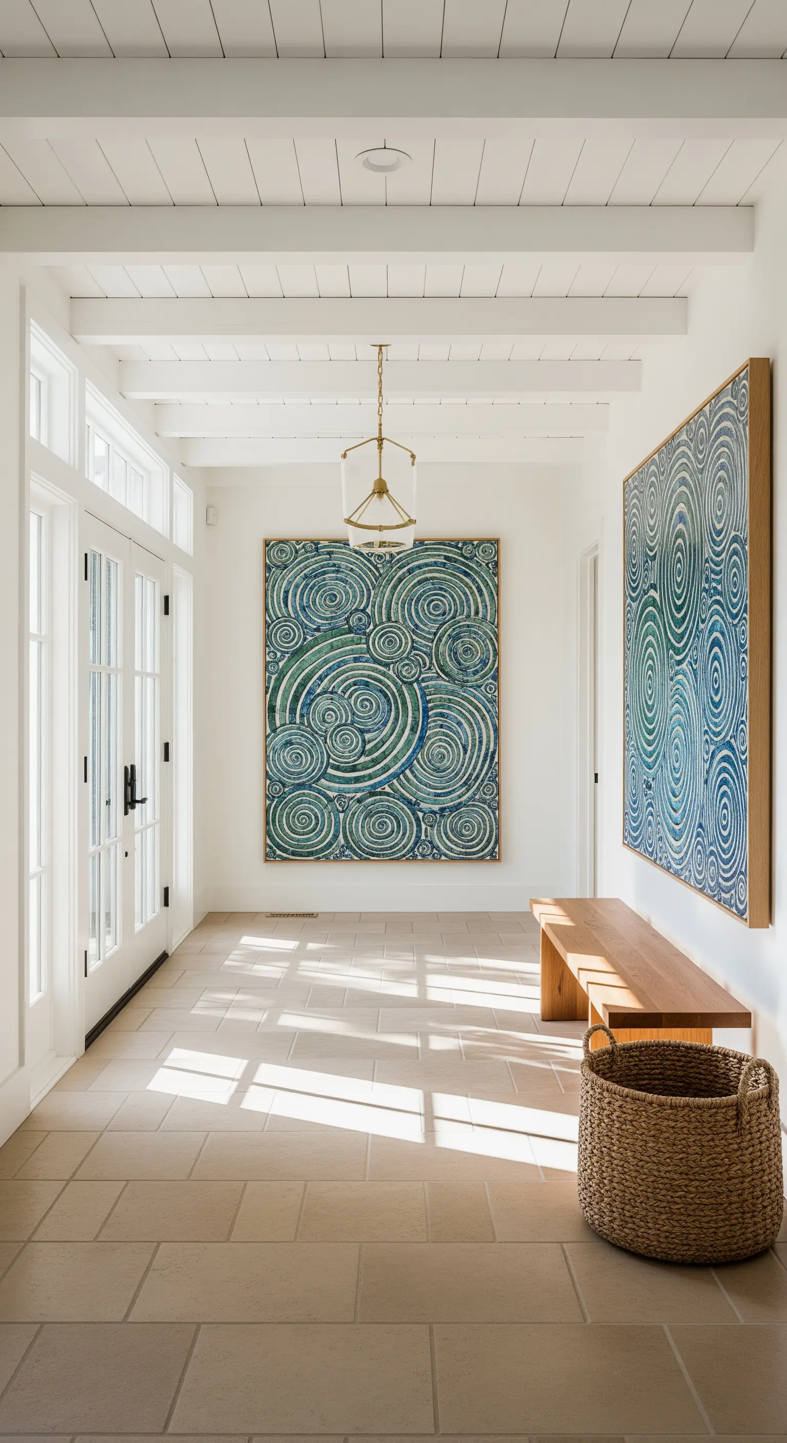 Ingresso luminoso con grandi quadri astratti blu e verdi, panca in legno e pavimento chiaro.