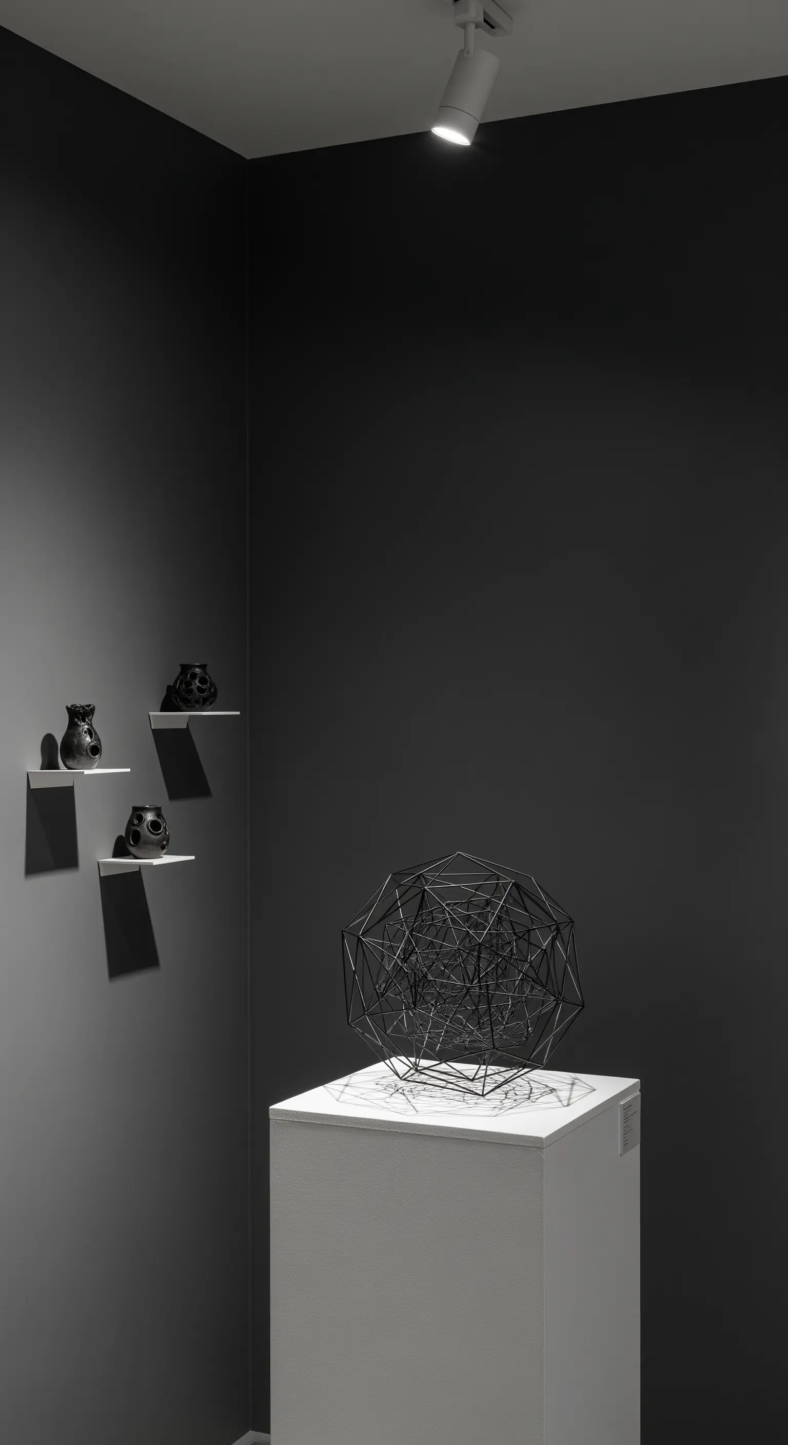 Scultura geometrica nera su piedistallo bianco illuminata da un faretto.