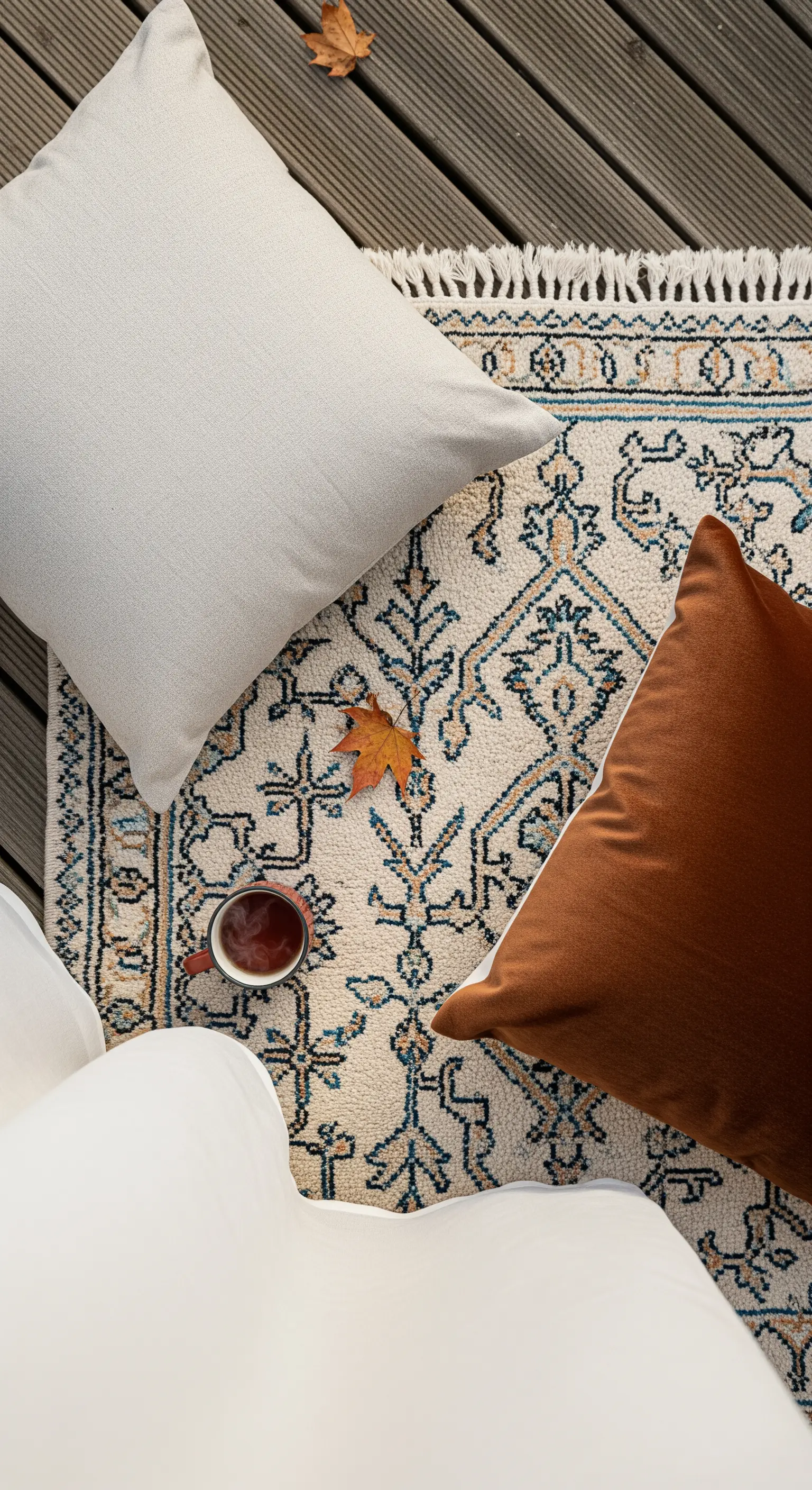 Dettaglio di un cuscino bianco e uno terracotta su un tappeto con motivi blu.