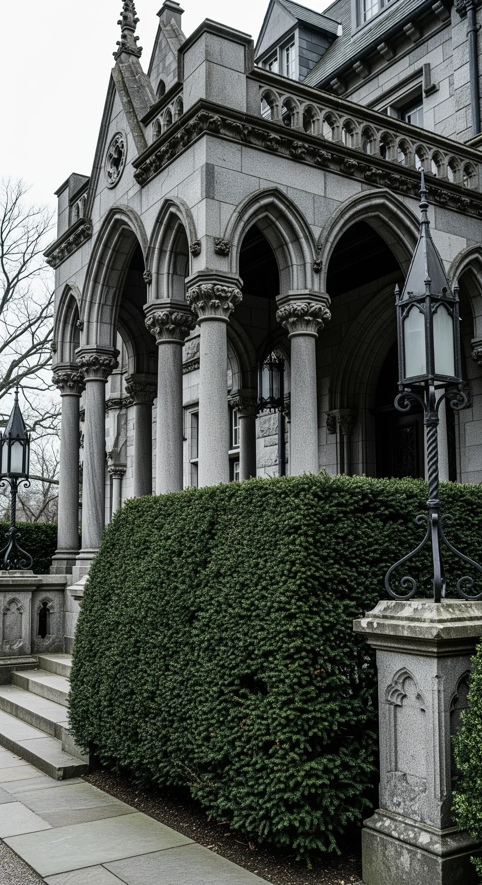 Ingresso in stile neogotico con archi a sesto acuto, colonne in pietra e una fitta siepe verde