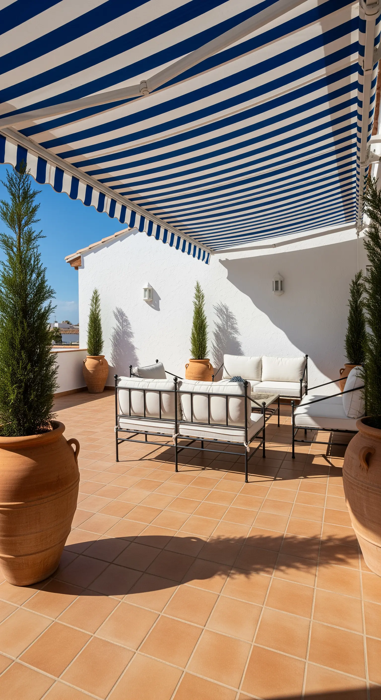 Terrazza in stile mediterraneo con tenda a righe bianche e blu, arredi bianchi e vasi in terracotta.