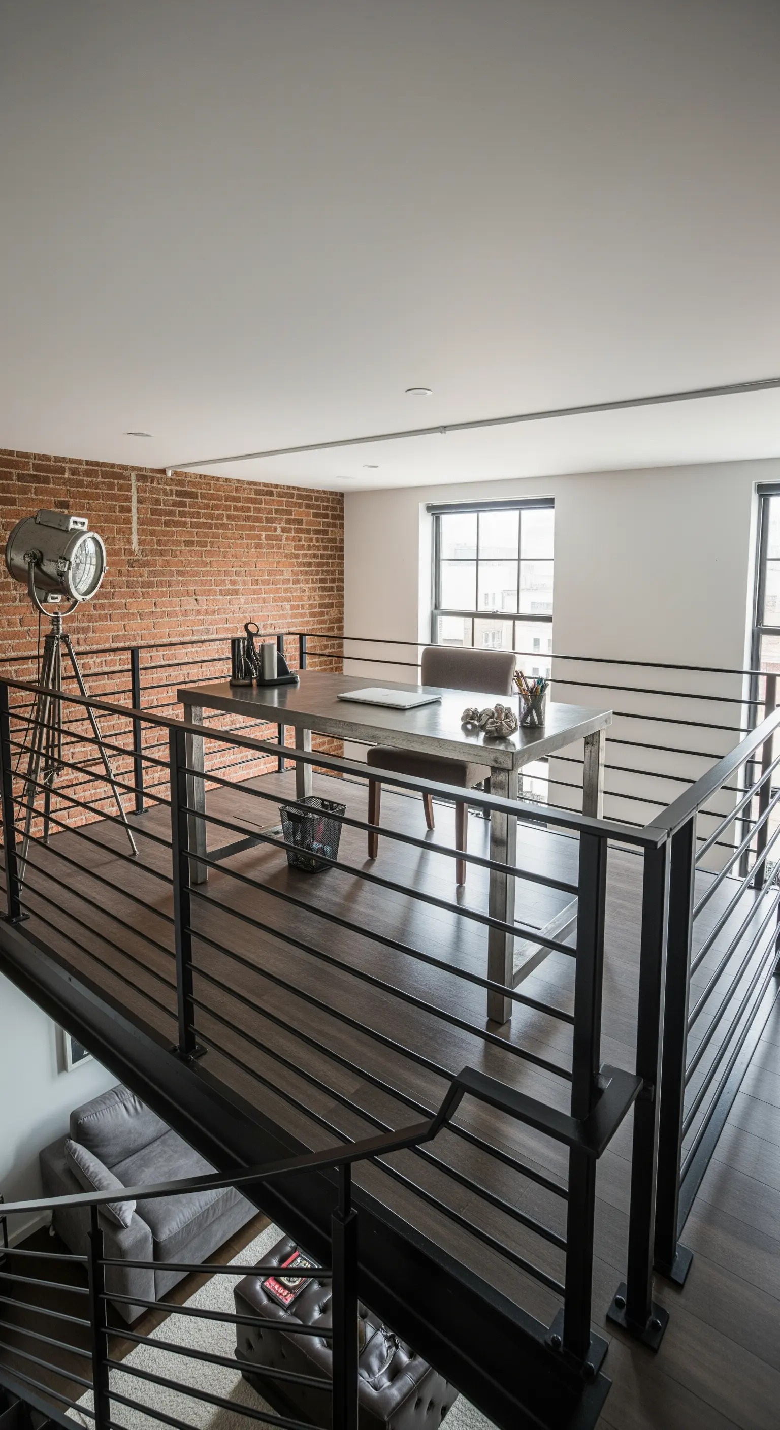 Ufficio su un soppalco in un loft, con ringhiera in metallo e parete di mattoni.
