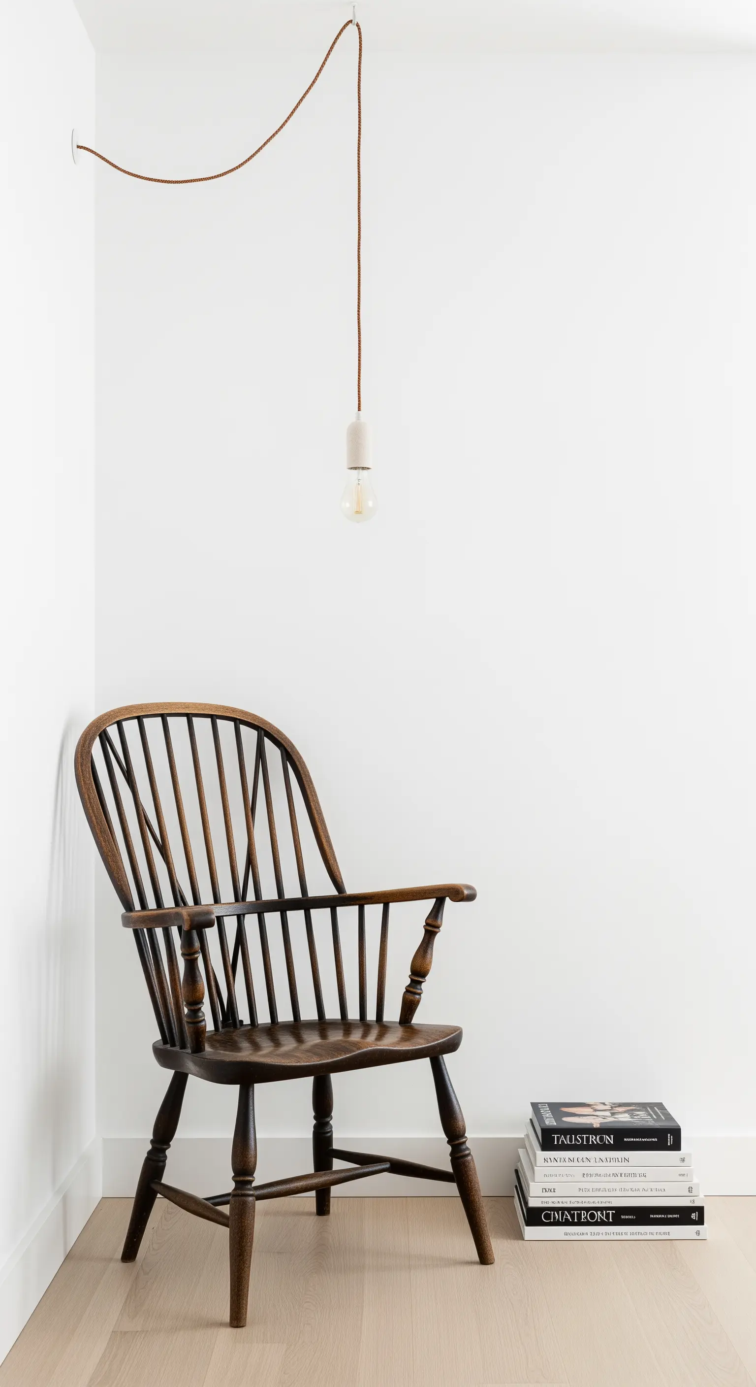 Sedia Windsor vintage in un angolo bianco minimalista con una lampadina appesa.