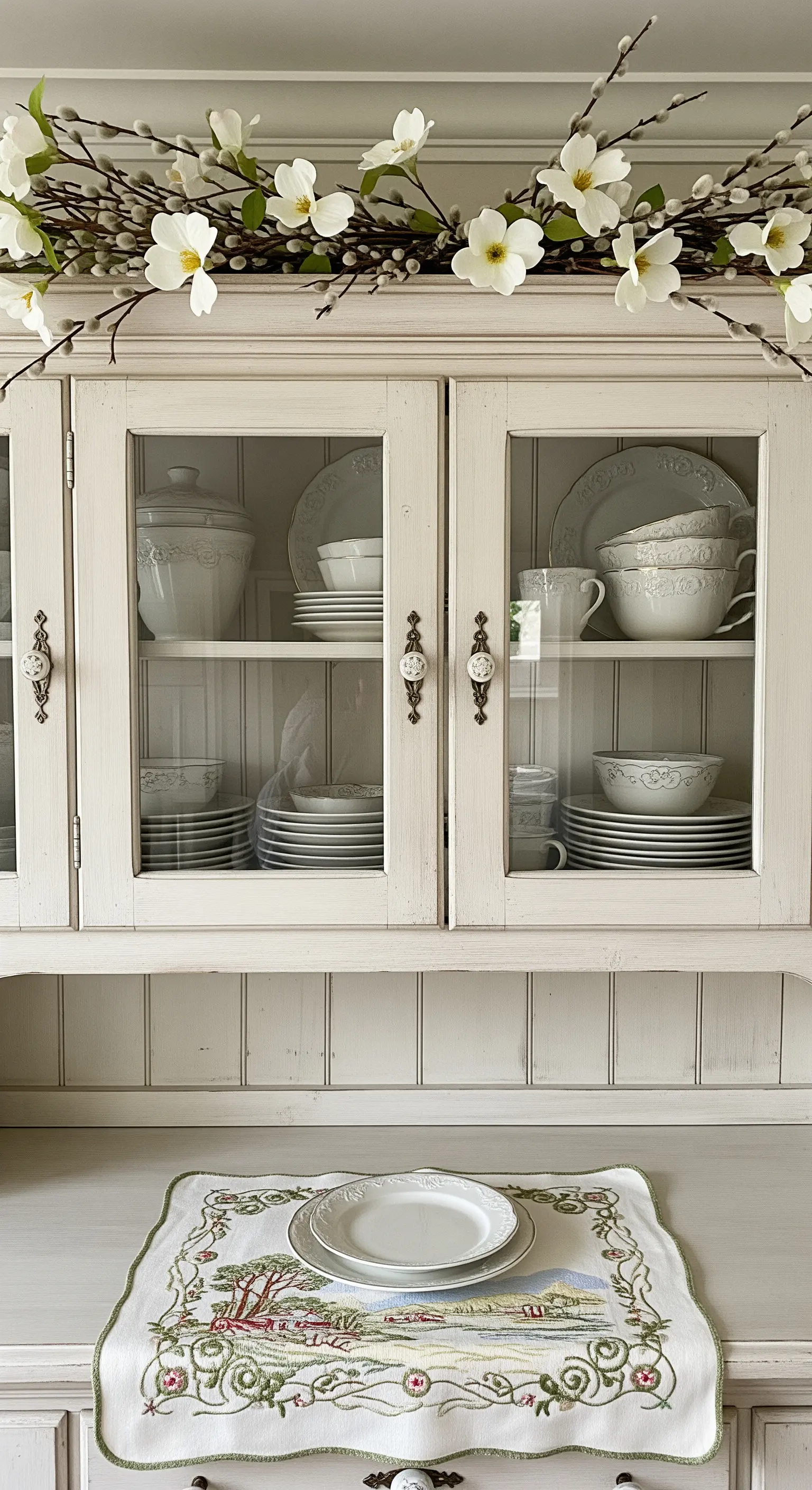 Credenza shabby chic bianca decorata con una ghirlanda di rami di salice e fiori bianchi.