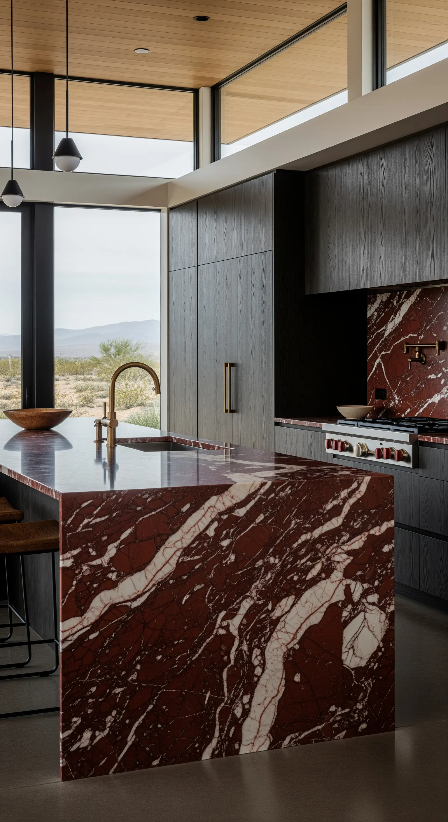 Isola cucina monolitica in marmo rosso intenso con venature bianche, accostata a mobili neri.