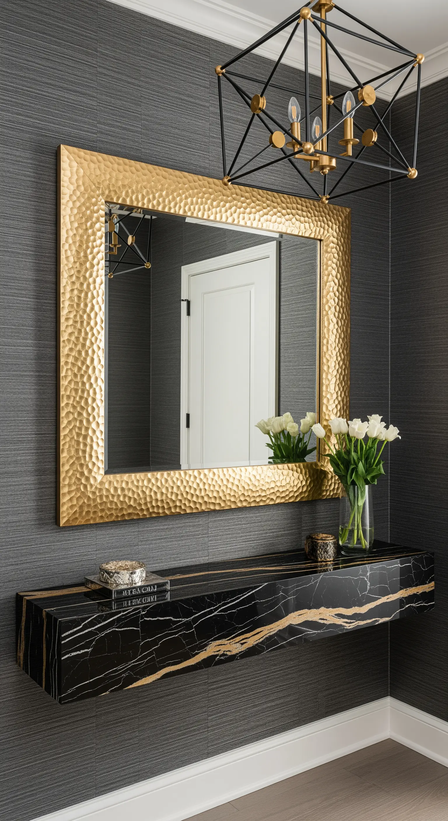 Ingresso con parete grigia texturizzata, specchio in oro martellato e consolle sospesa in marmo nero.