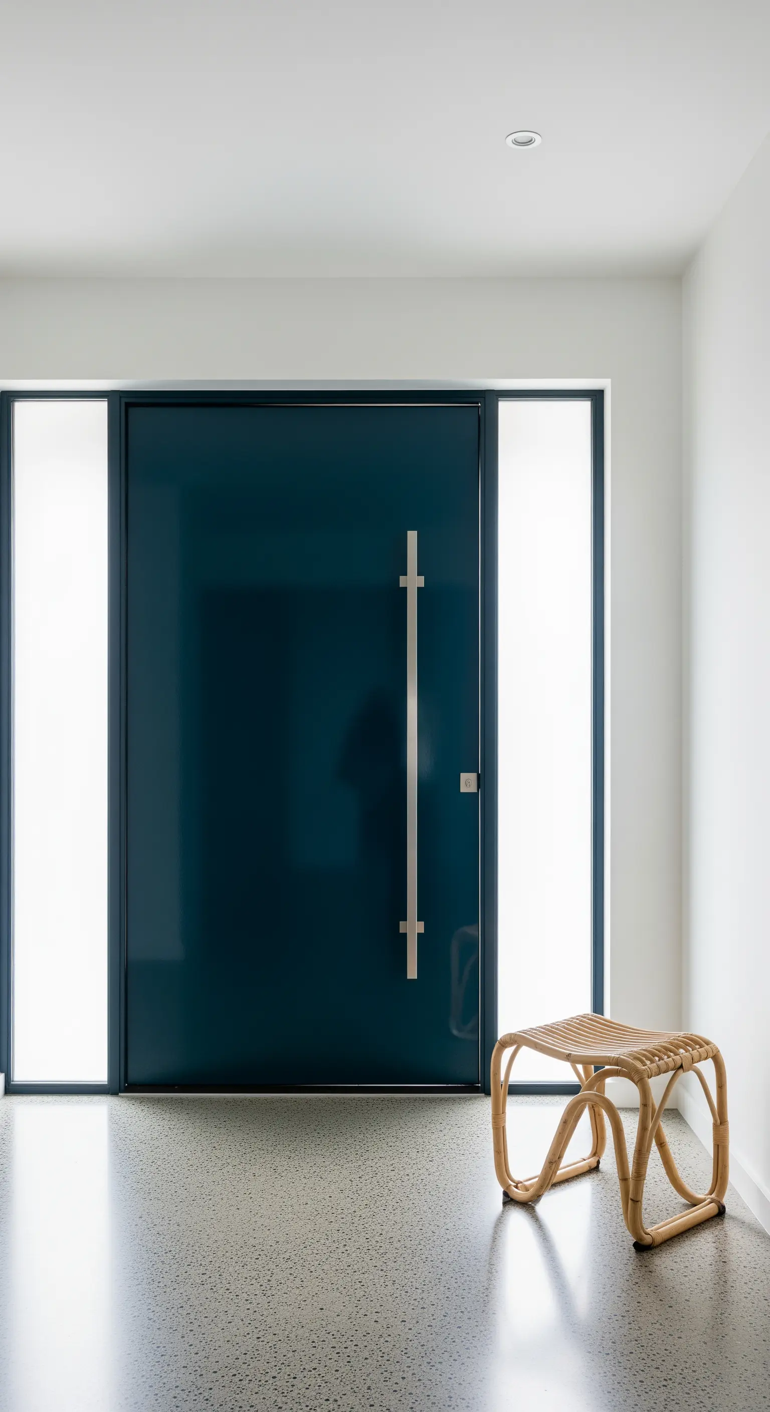 Porta d'ingresso moderna color petrolio con accanto un piccolo sgabello in rattan.