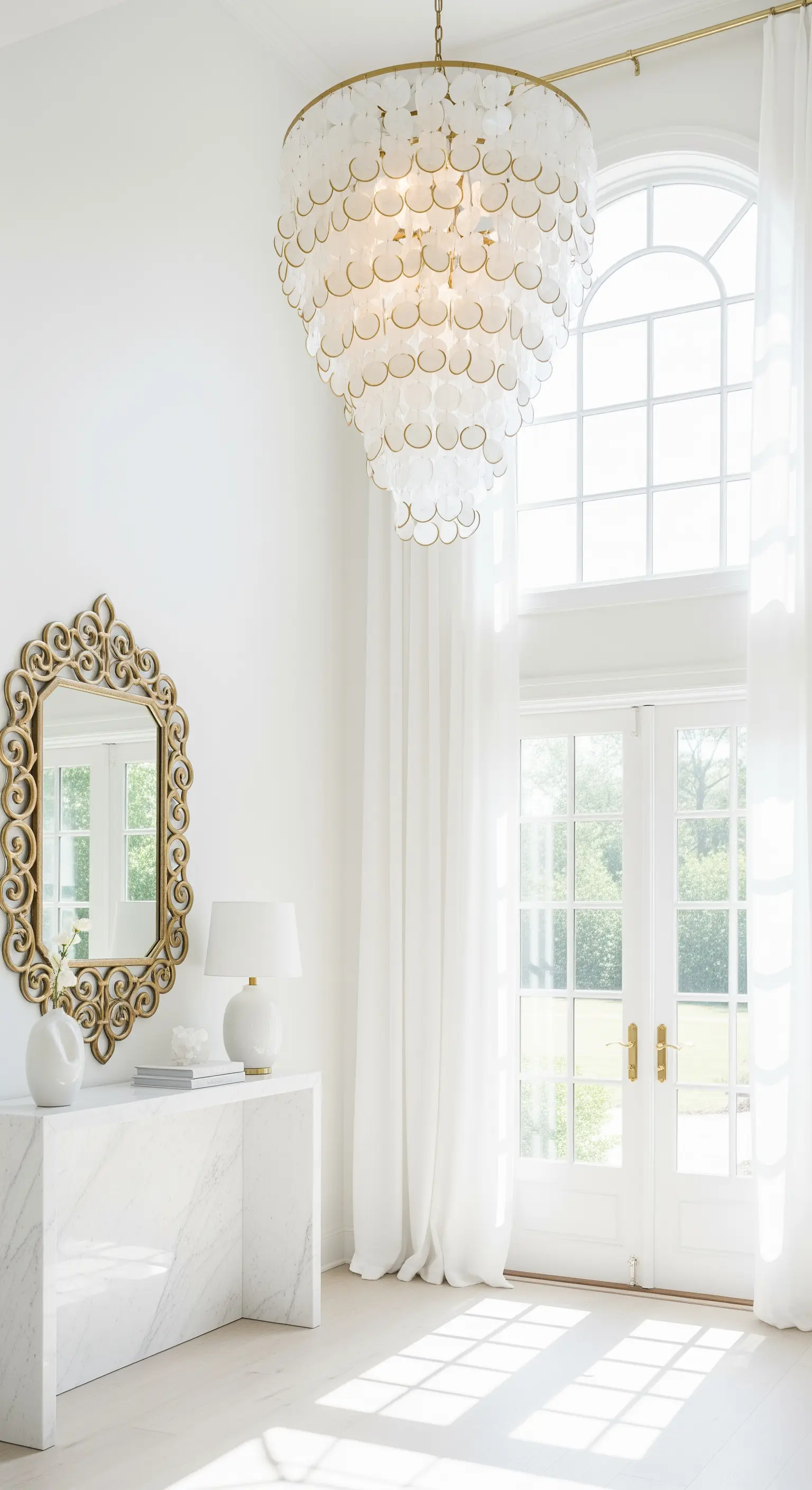 Ingresso luminoso a doppia altezza con lampadario in madreperla e specchio dorato.